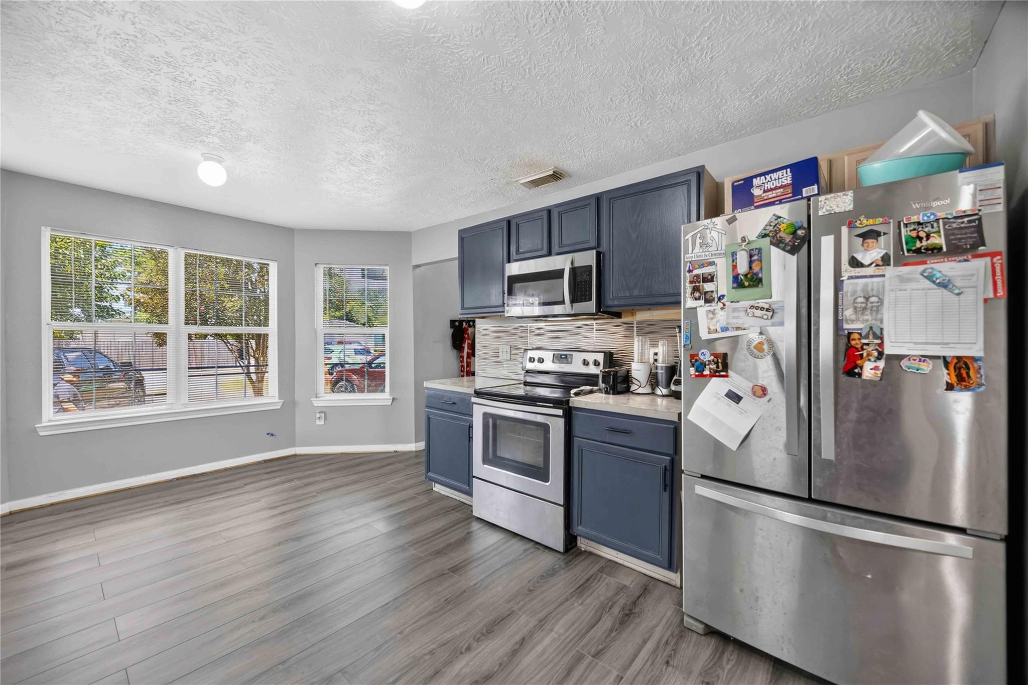 Kitchen with dark blue cabinets, stainless steel appliances, and three windows.