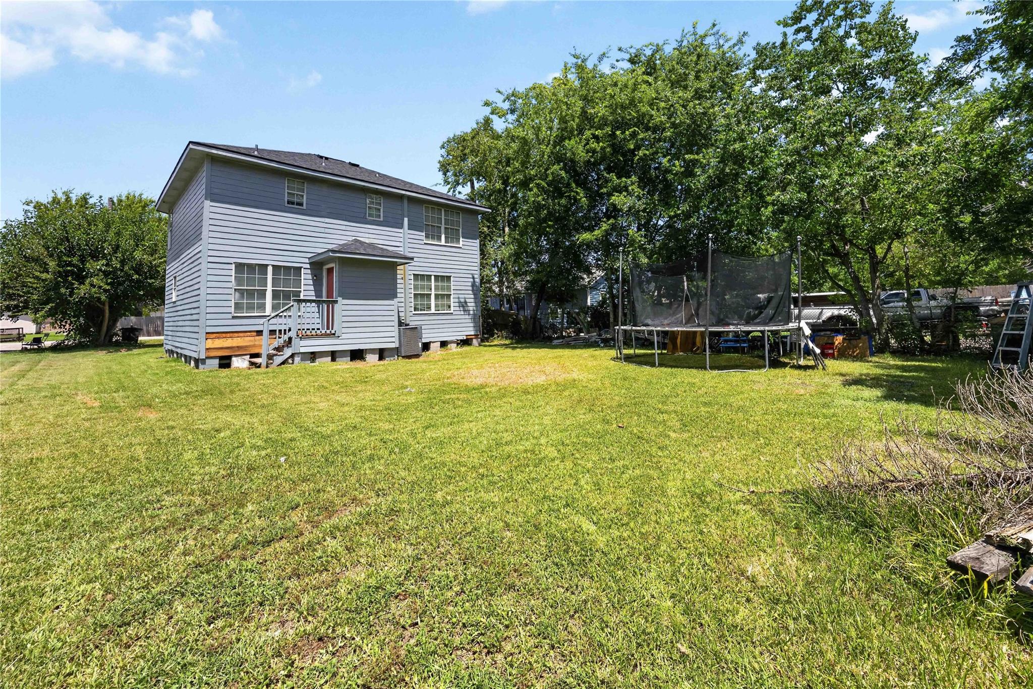 Two-story gray house beside a broad grassy backyard with a raised deck and trampoline.