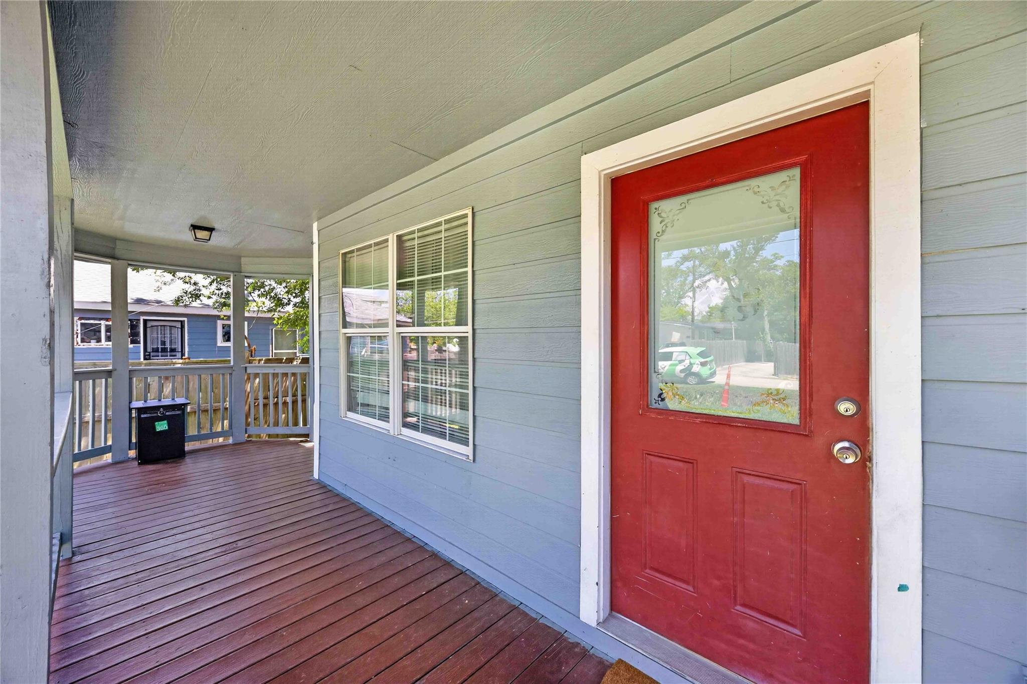 Covered front porch with a red entry door, blue-gray siding, and dark wood decking.