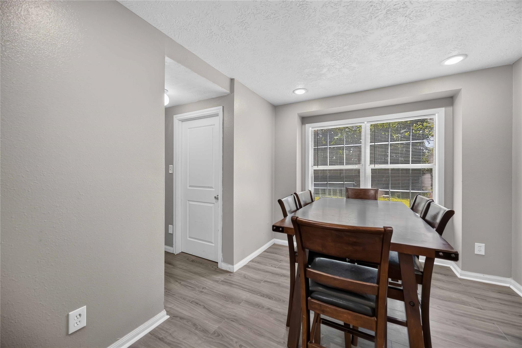Dining room with a dark wood table and chairs beside a wide window with blinds.