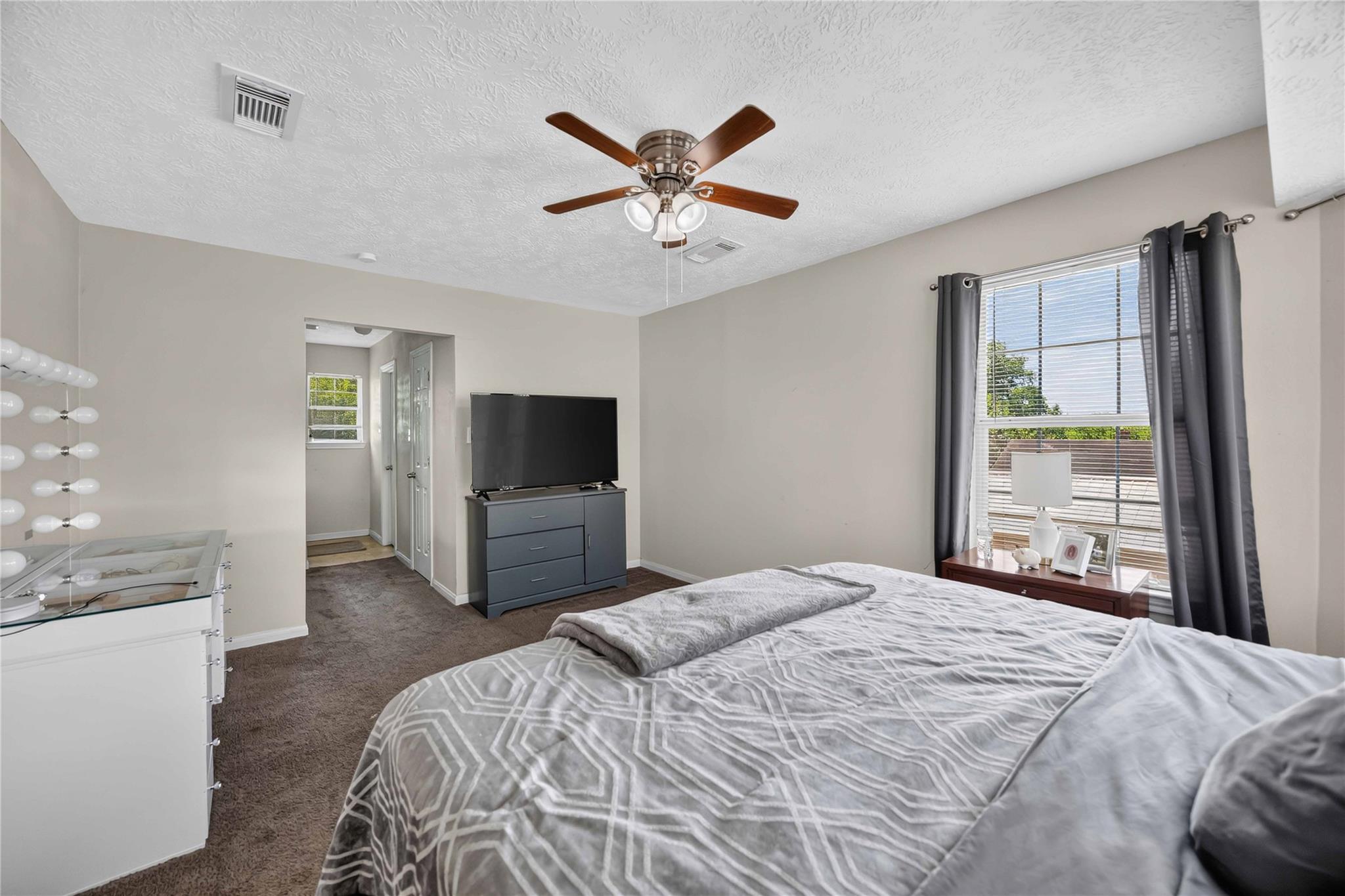 Bedroom with gray geometric bedding, a ceiling fan, and a window with dark curtains.