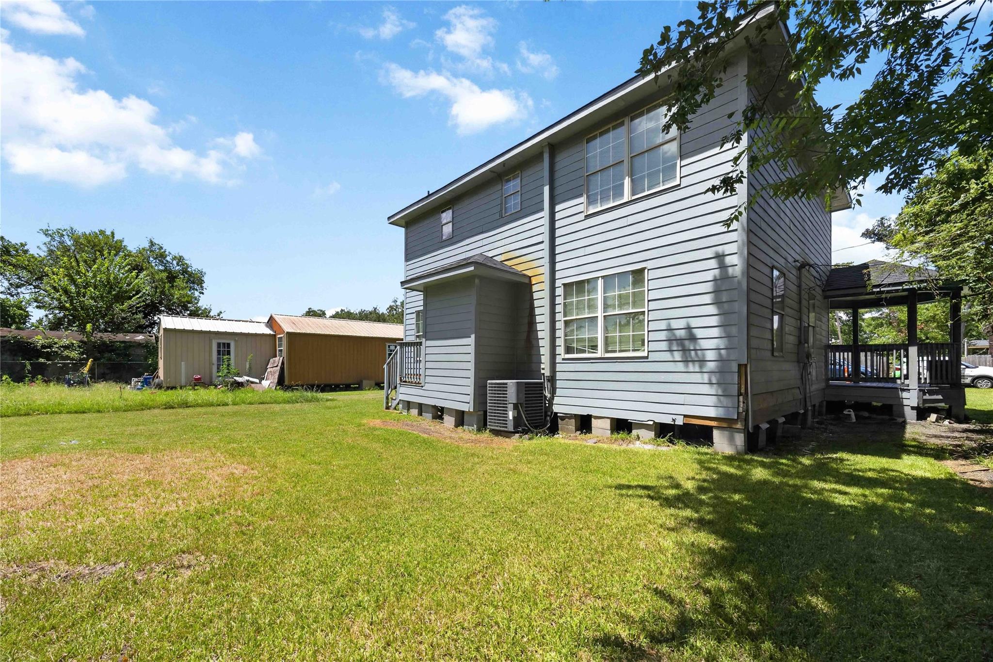 Gray two-story house with a covered deck, broad grassy yard, and two outbuildings.