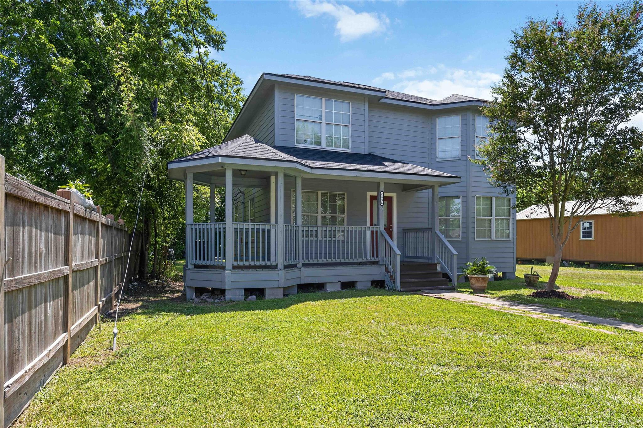 Two-story gray house with a covered porch and fenced grassy yard.