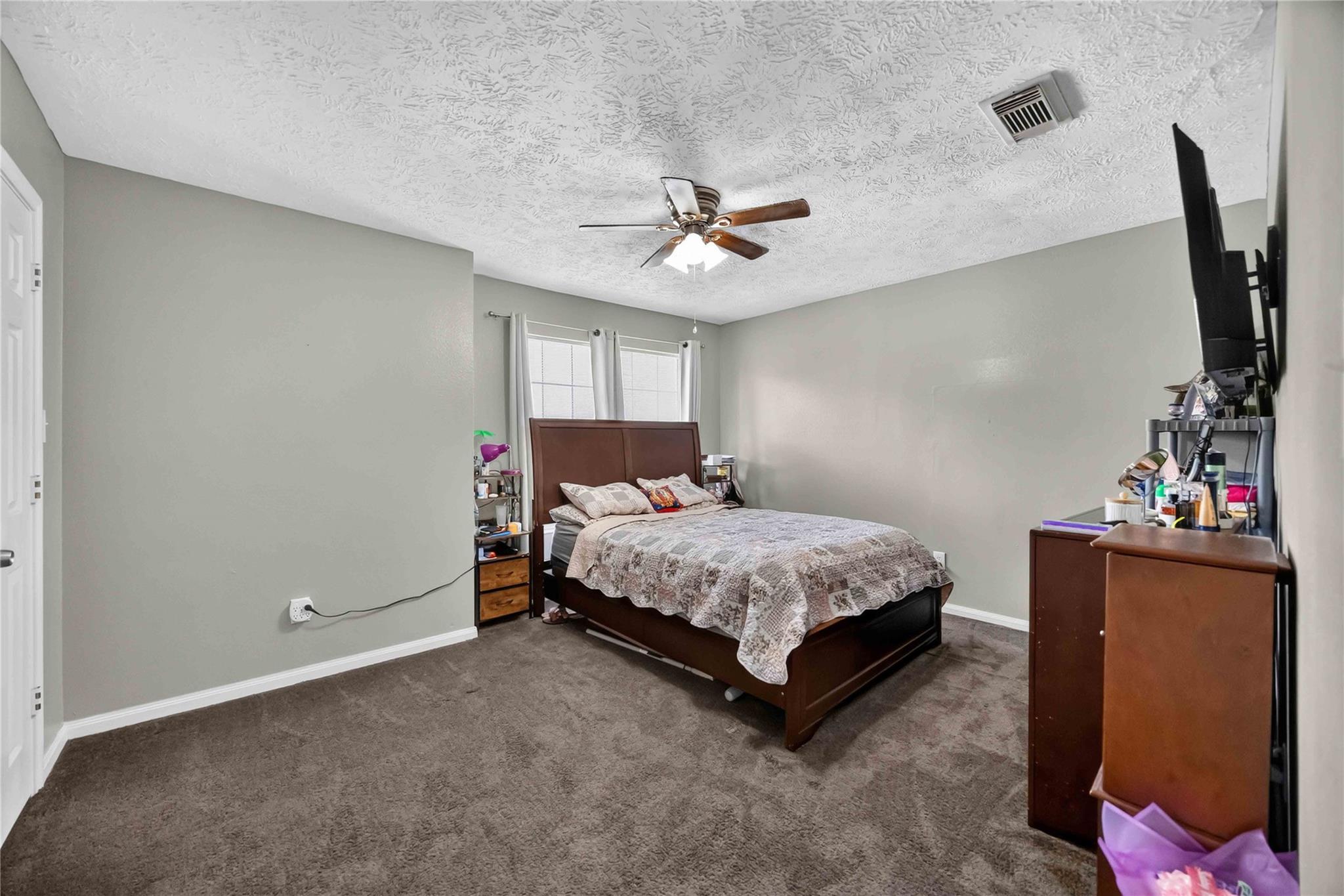 Bedroom with a brown wood bed, patterned bedding, gray walls, and brown carpet.