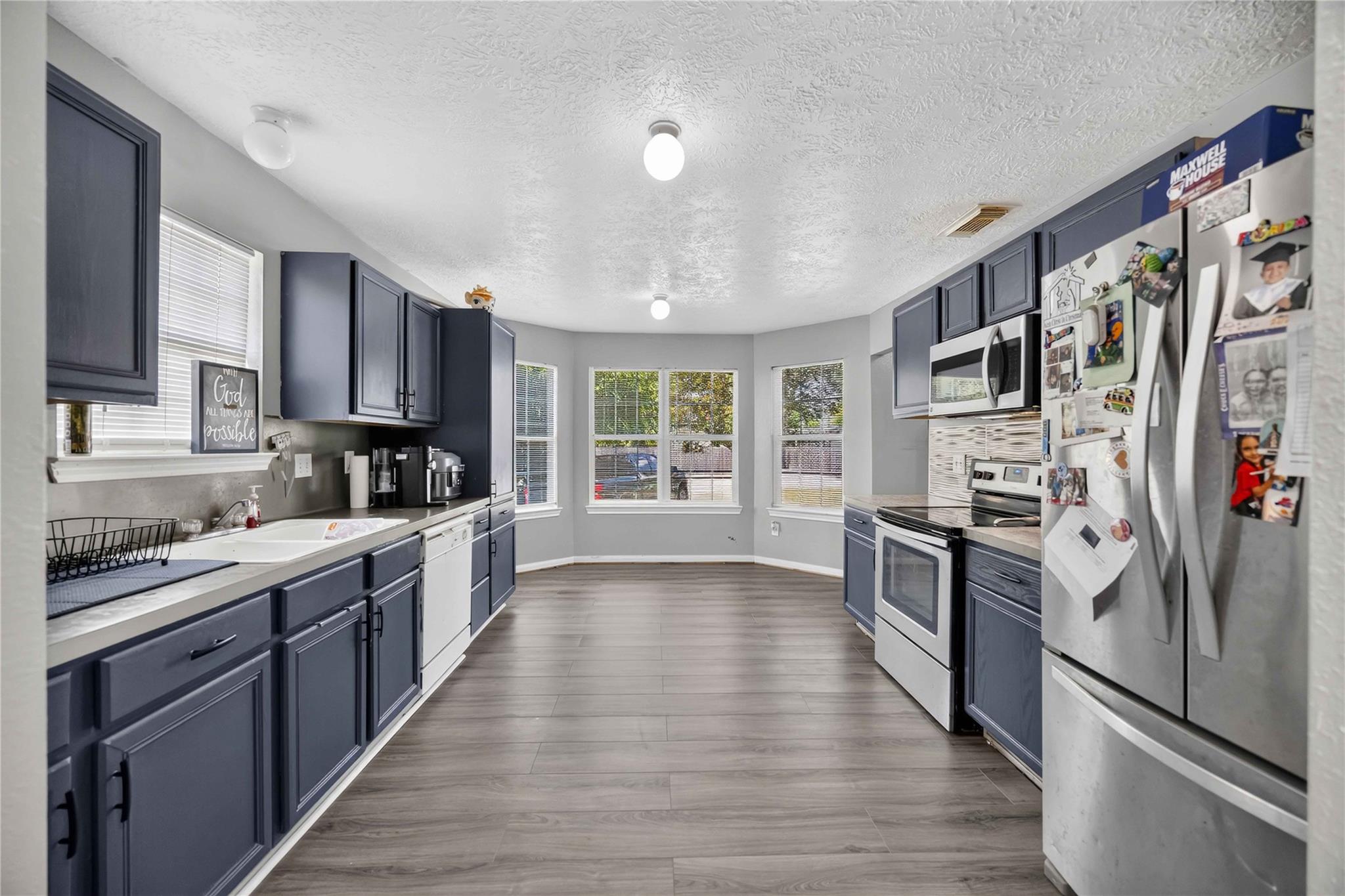 Kitchen with dark blue cabinets, stainless steel appliances, and a row of windows at the far end.