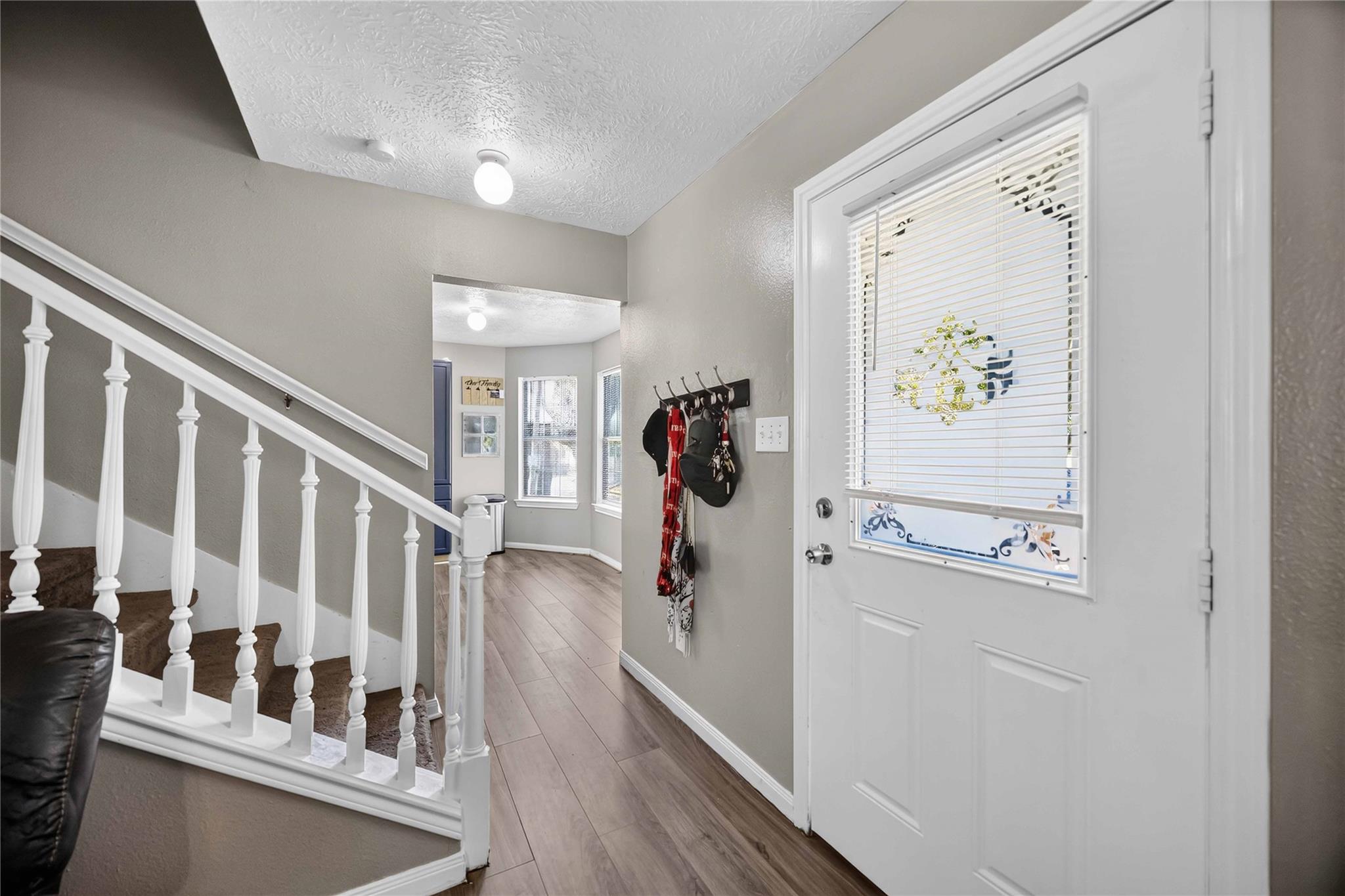 Entry hall with a white staircase, wood-look floors, and a front door with blinds.