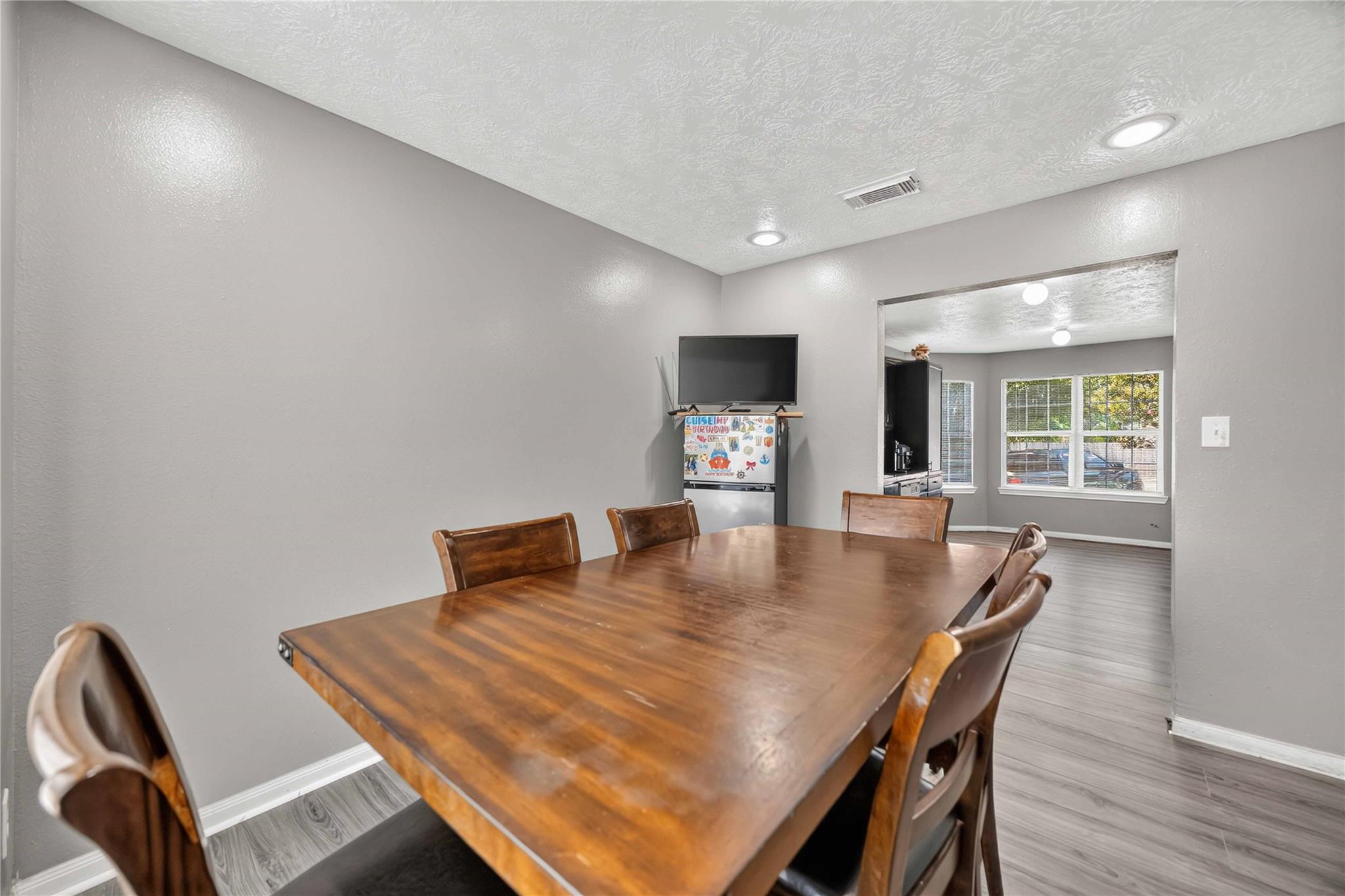 Dining area with a large wooden table and chairs, opening into a bright room with wide windows.
