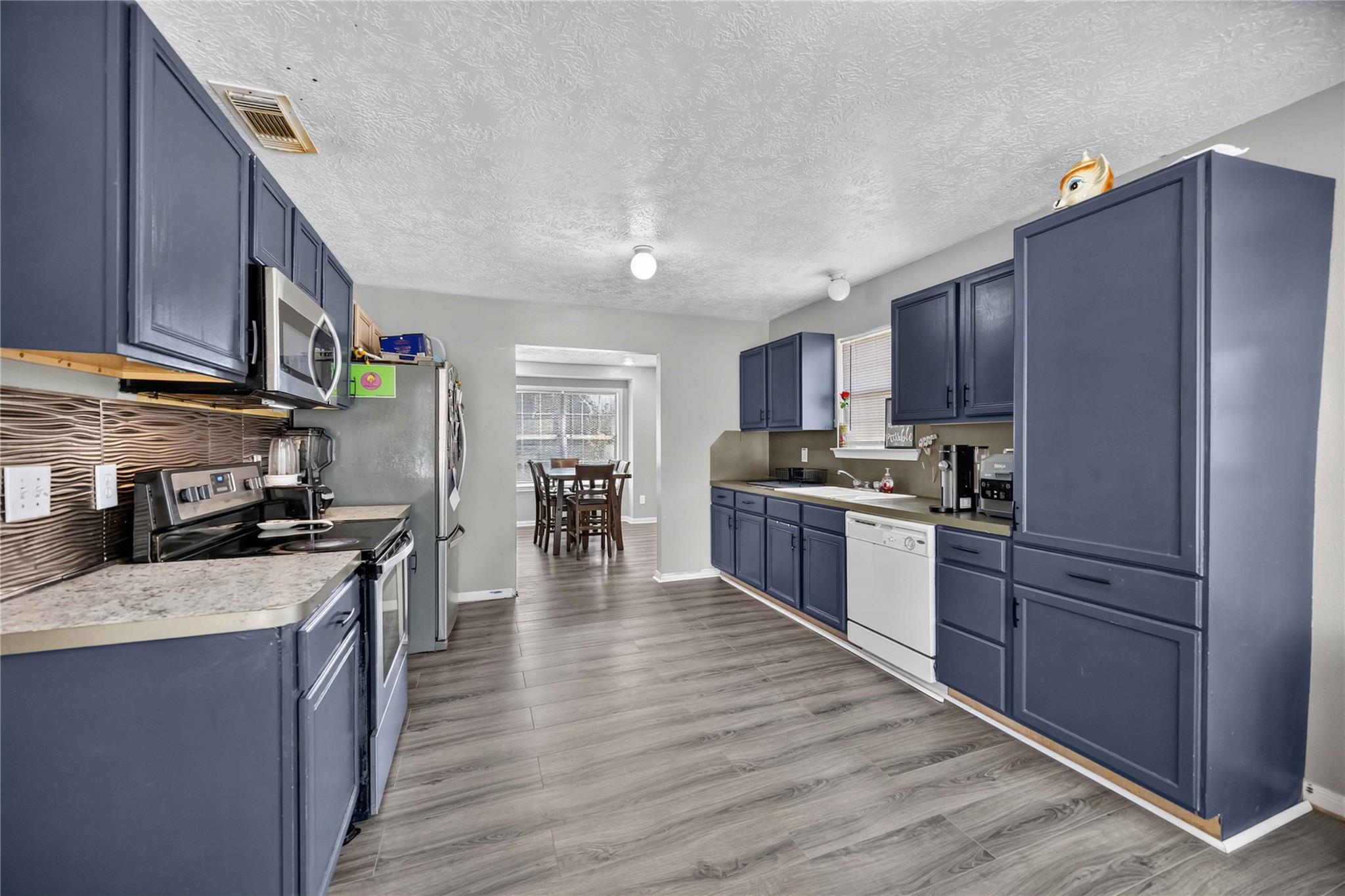 Kitchen with dark blue cabinets, stainless steel appliances, and an opening to a dining area.