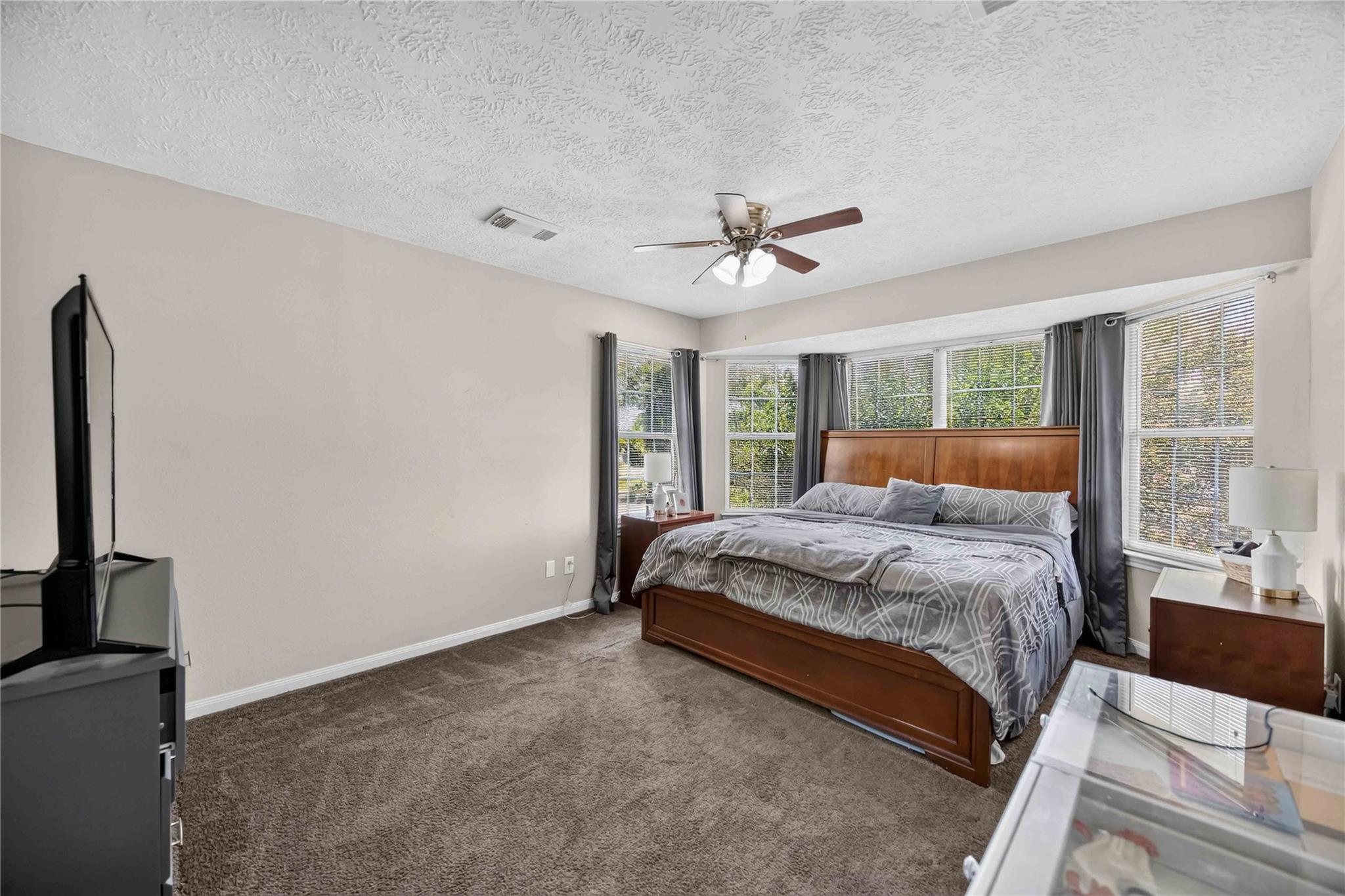 Furnished bedroom with a wooden bed, gray patterned bedding, and windows along the back wall.