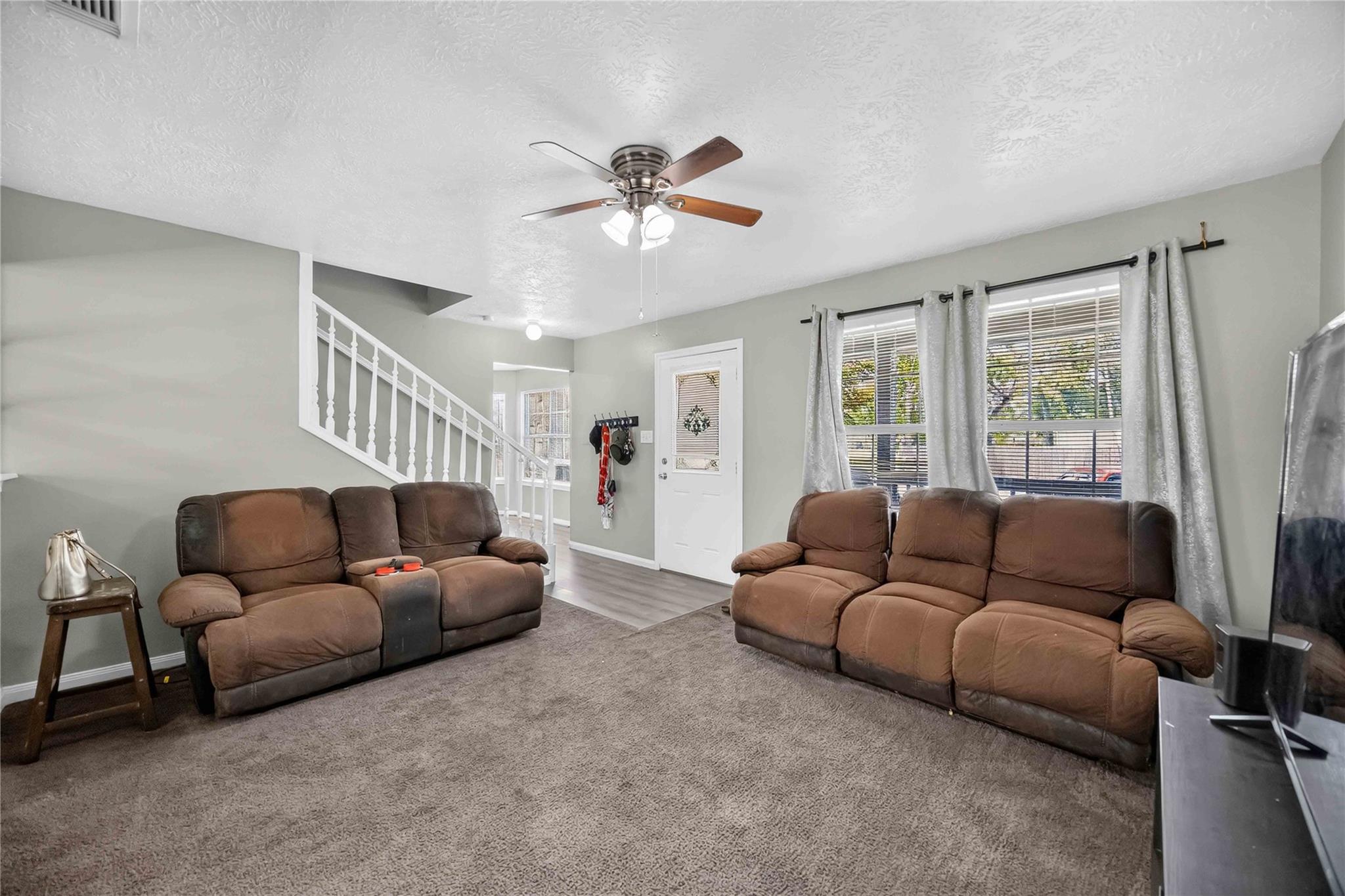 Living room with two brown reclining sofas, gray carpet, and a staircase beside the front door.