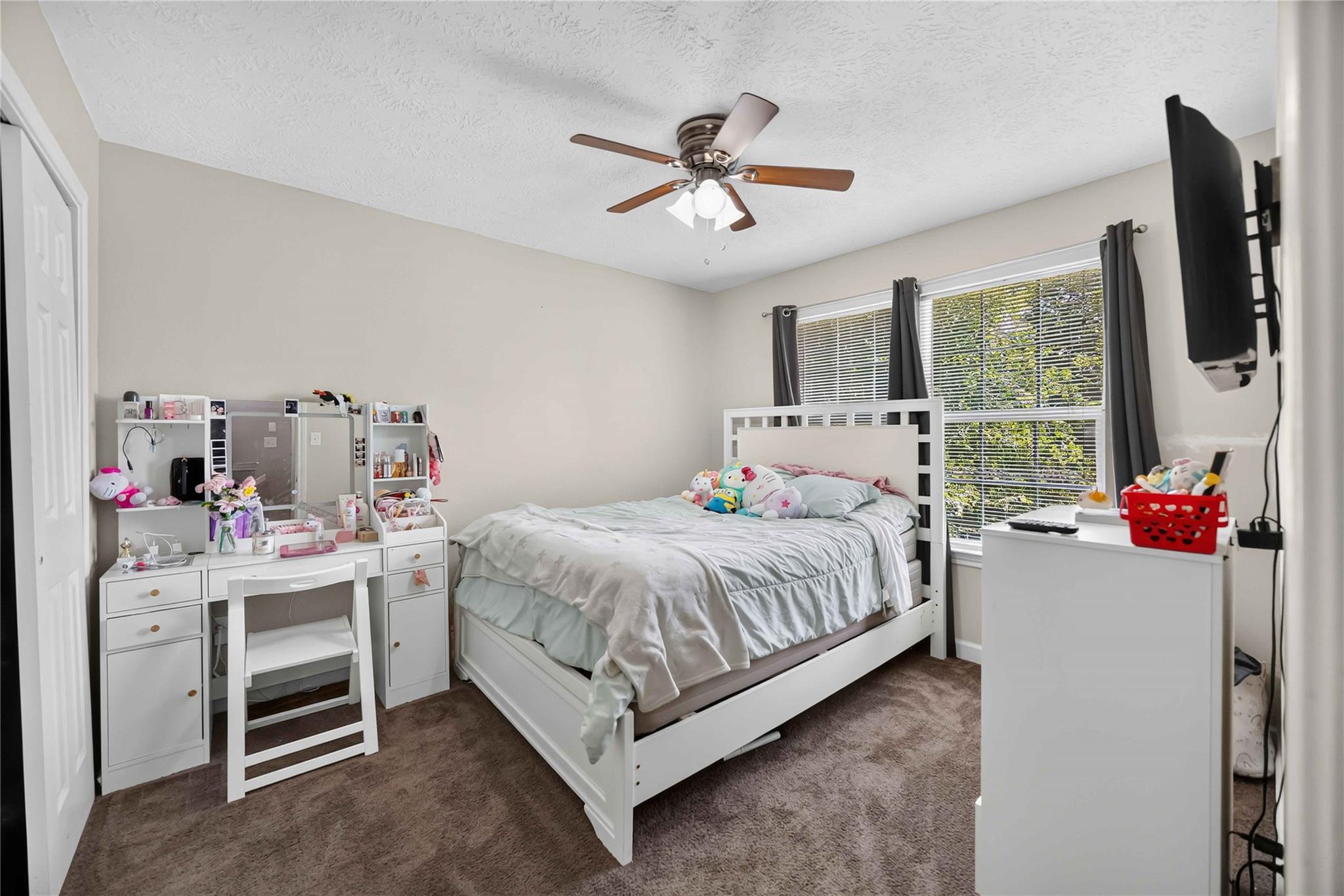 Bedroom with a white bed, plush toys, vanity, and a large curtained window.