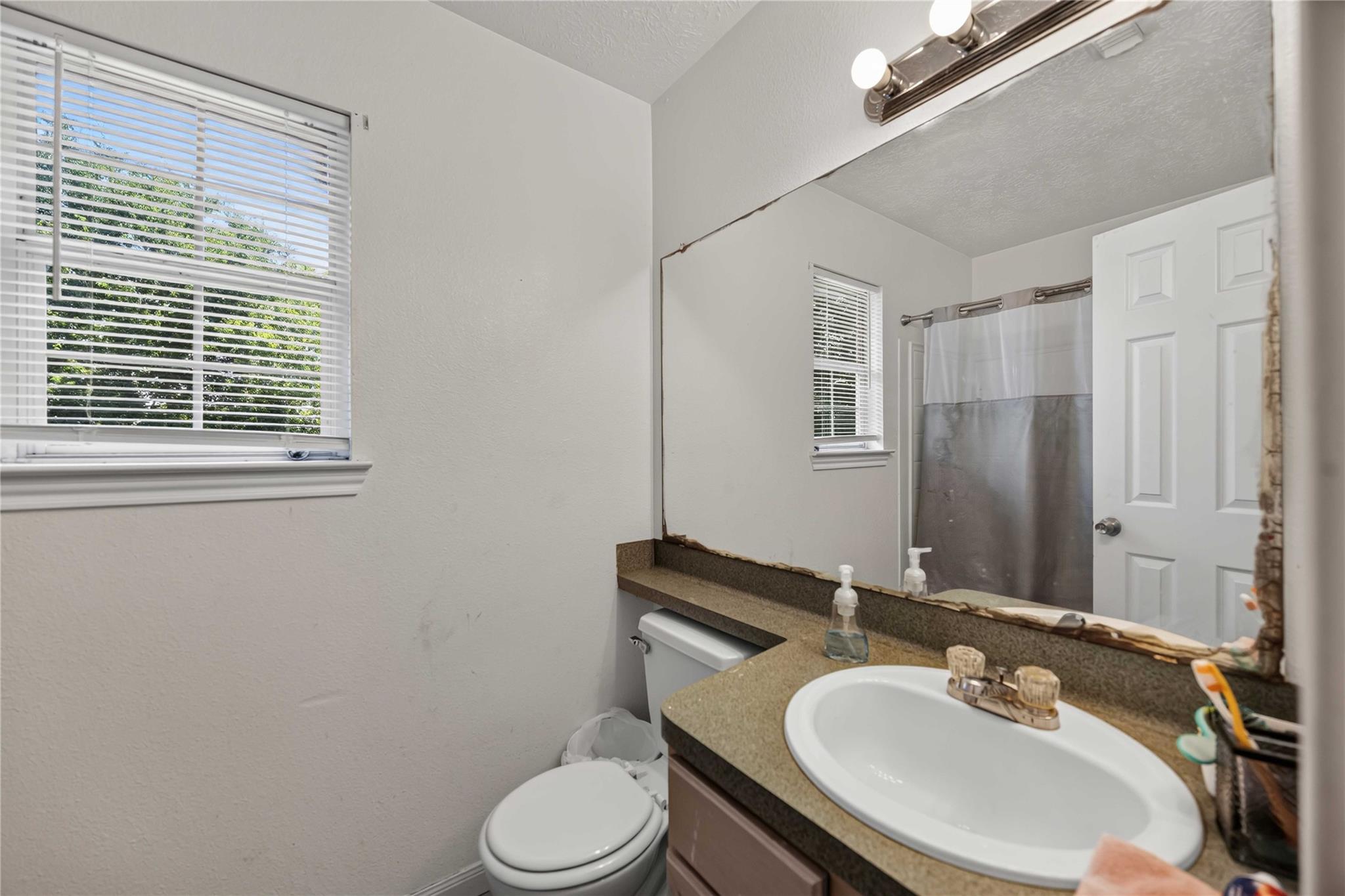 Bathroom with a sink, toilet, large mirror with damaged edges, and shower.