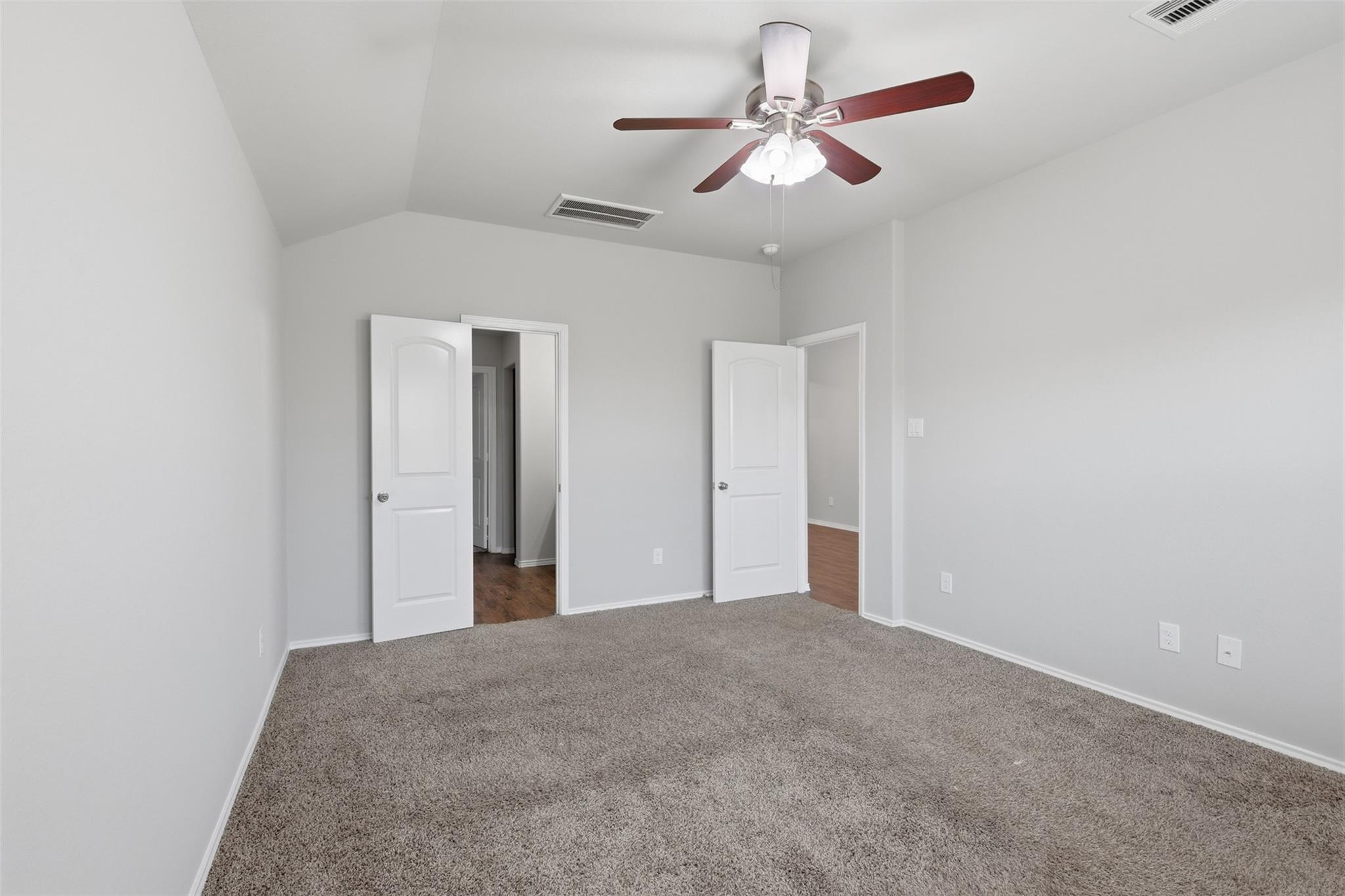 Empty bedroom with gray carpet, a vaulted ceiling, and a ceiling fan with lights.