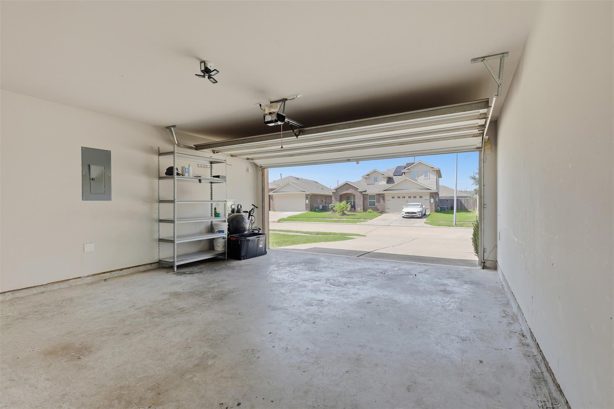 Mostly empty garage with the overhead door open and metal storage shelving along one wall.