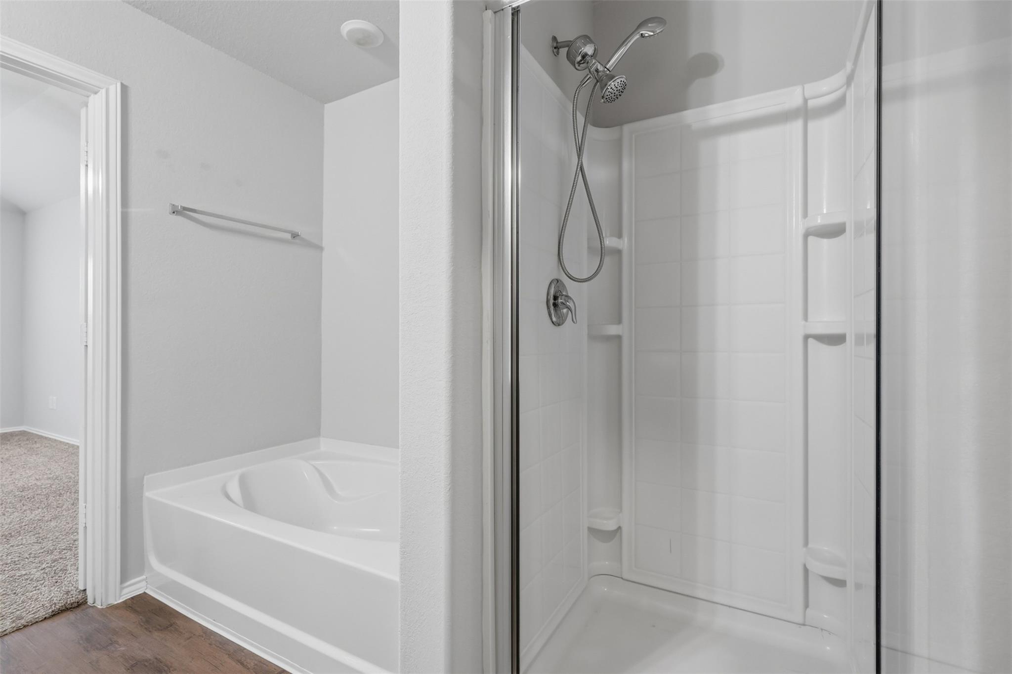 Bathroom with a white bathtub beside a glass-enclosed shower with chrome fixtures and built-in shelves.