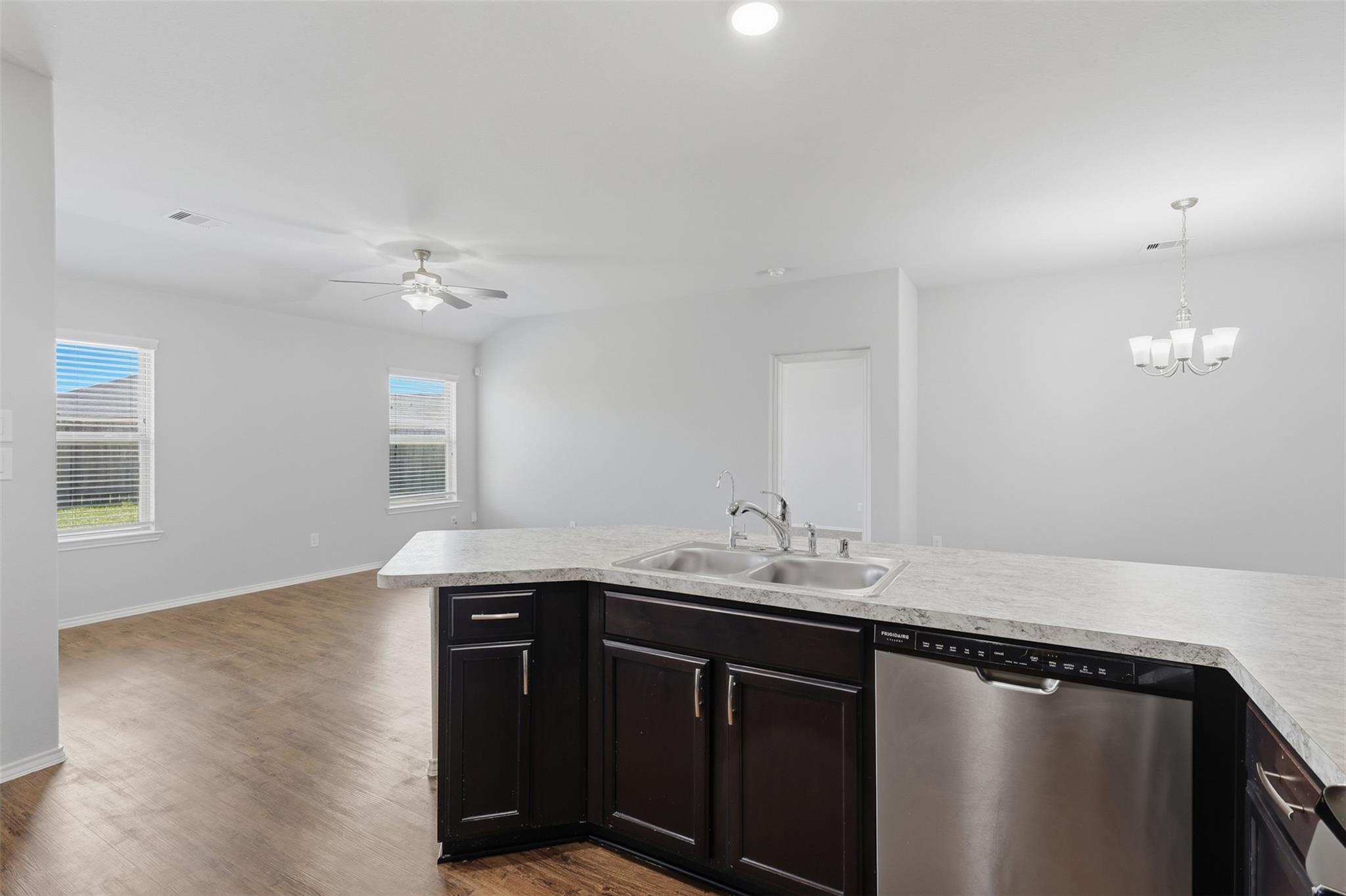 Vacant kitchen with dark cabinets, light stone island countertop, double sink, and stainless steel dishwasher.