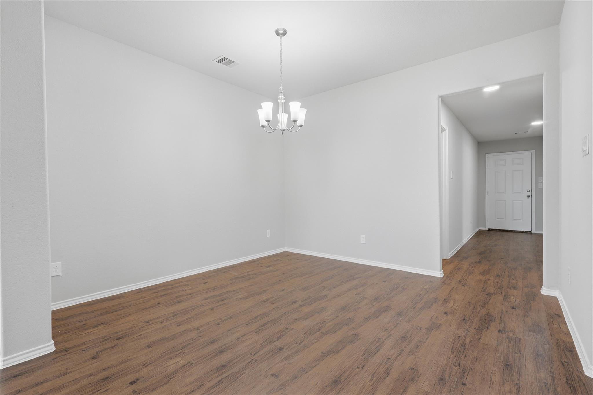 Empty dining room with wood-look floors and a chandelier, viewed toward the entry hallway.