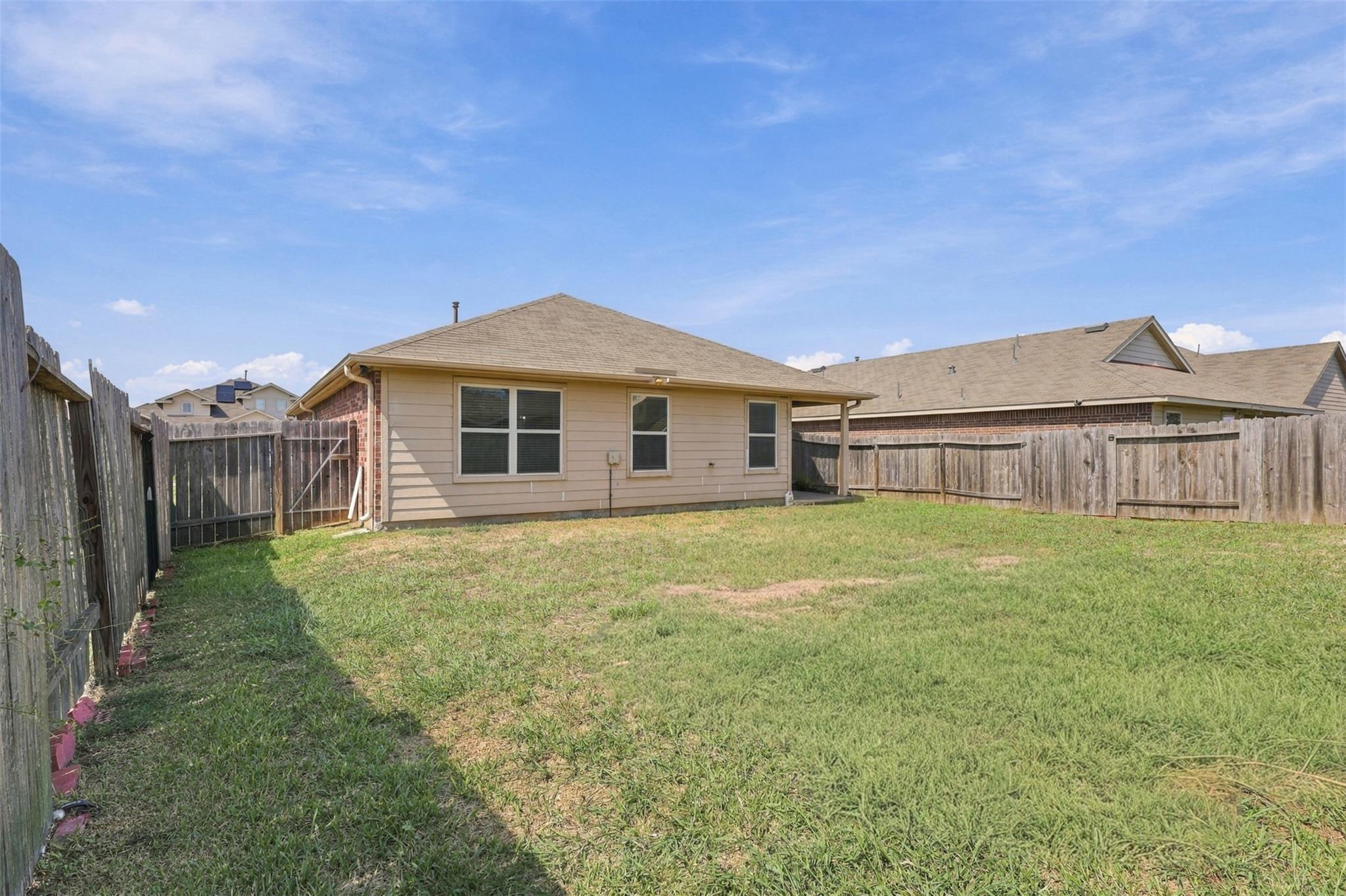 Home’s rear exterior and fenced grassy backyard with neighboring houses beyond.