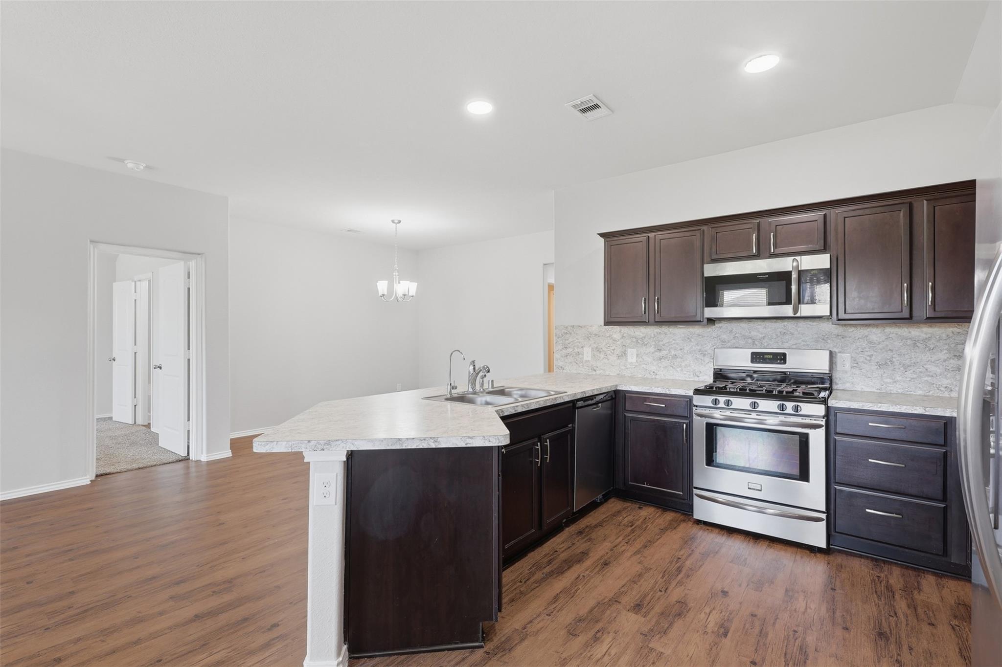 Kitchen with dark cabinets, stainless steel appliances, and a stone-topped peninsula.