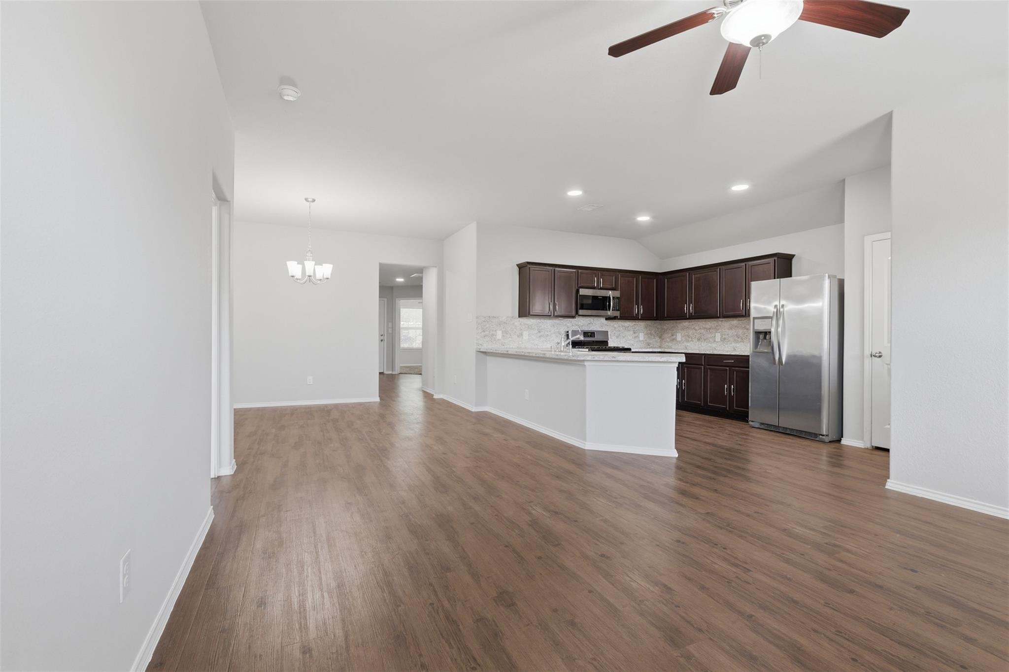 Open kitchen and dining area with dark cabinets, stainless appliances, and wood-look floors.