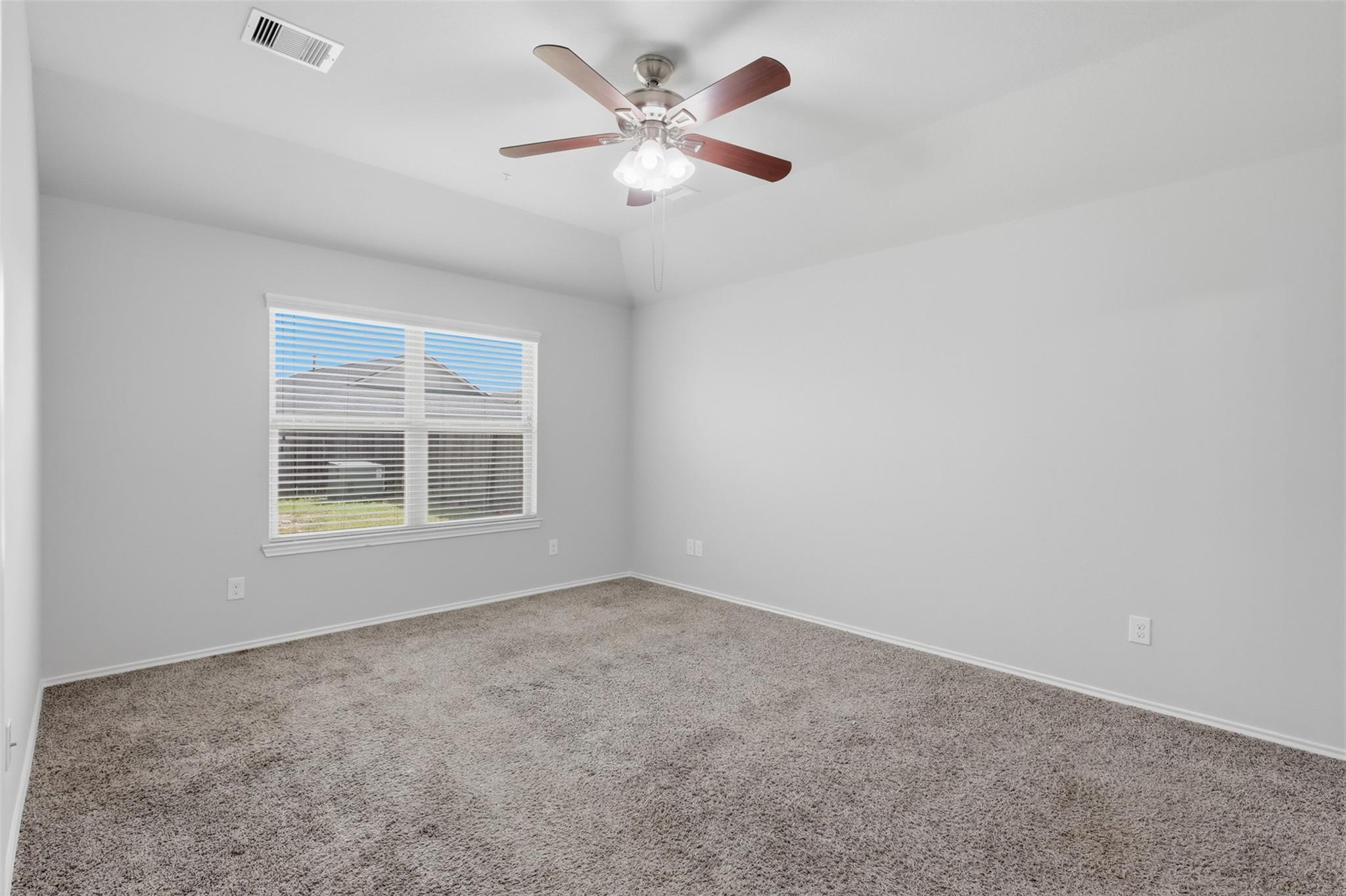 Empty bedroom with beige carpet, a ceiling fan, and a window with blinds.