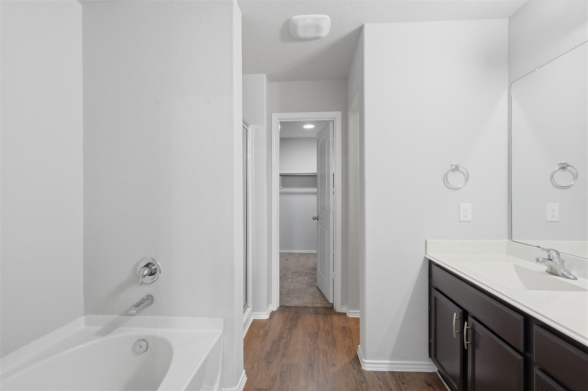 Bathroom with a white bathtub, dark wood vanity, and open doorway to a carpeted closet.