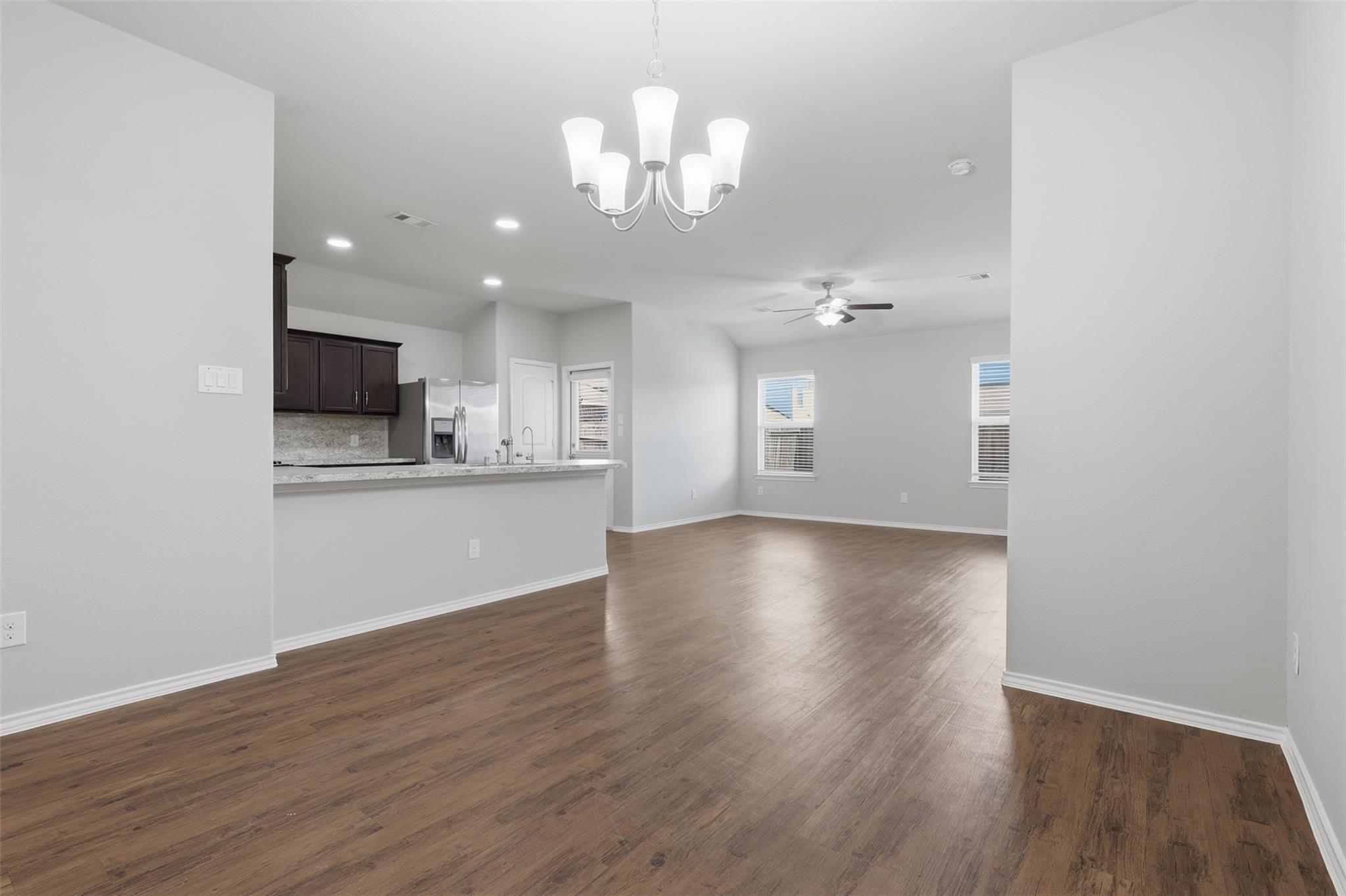 Open-plan kitchen and living area with dark cabinets, wood-look floors, and a chandelier.