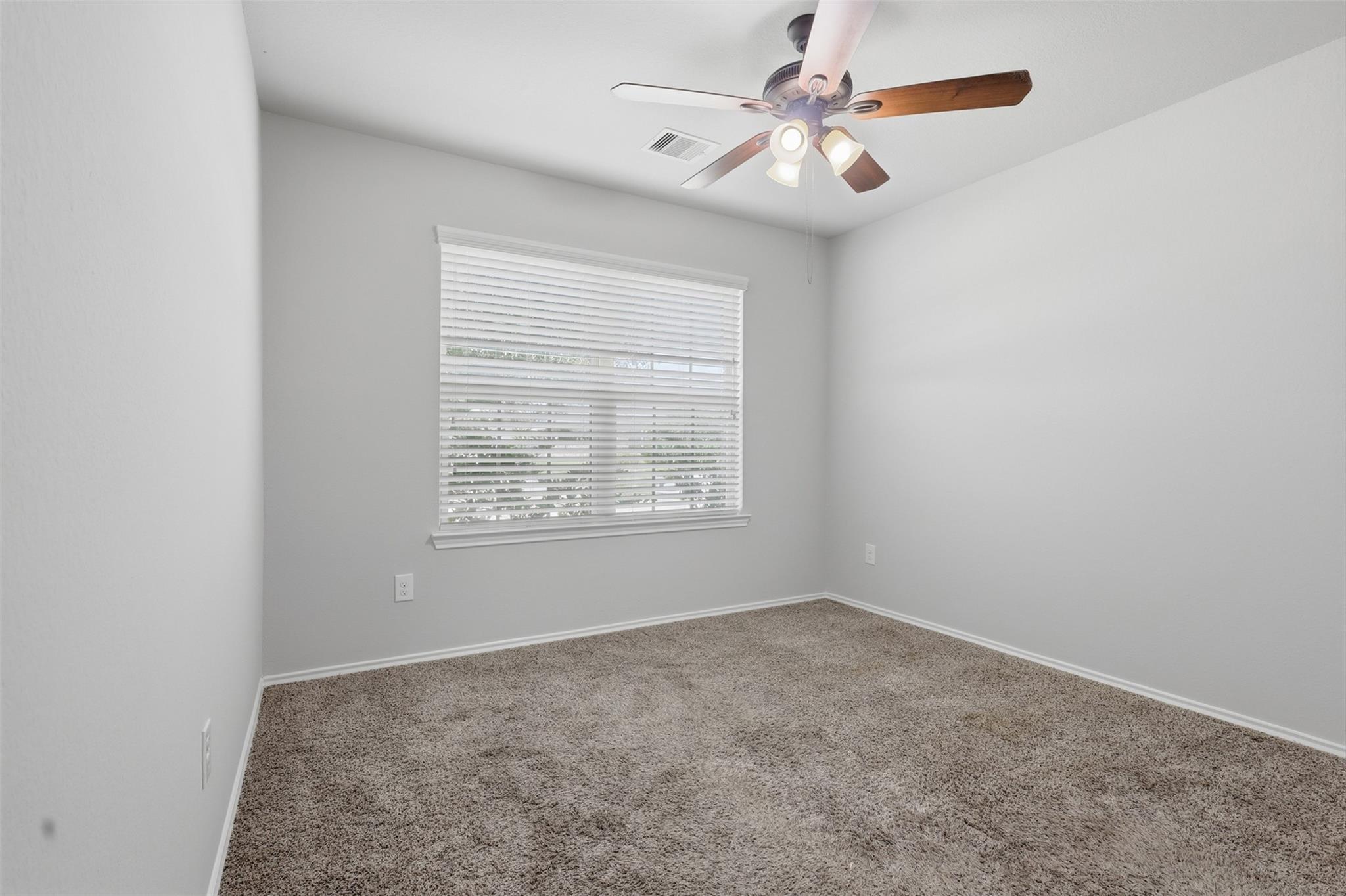 Empty bedroom with beige carpet, white window blinds, and a ceiling fan.