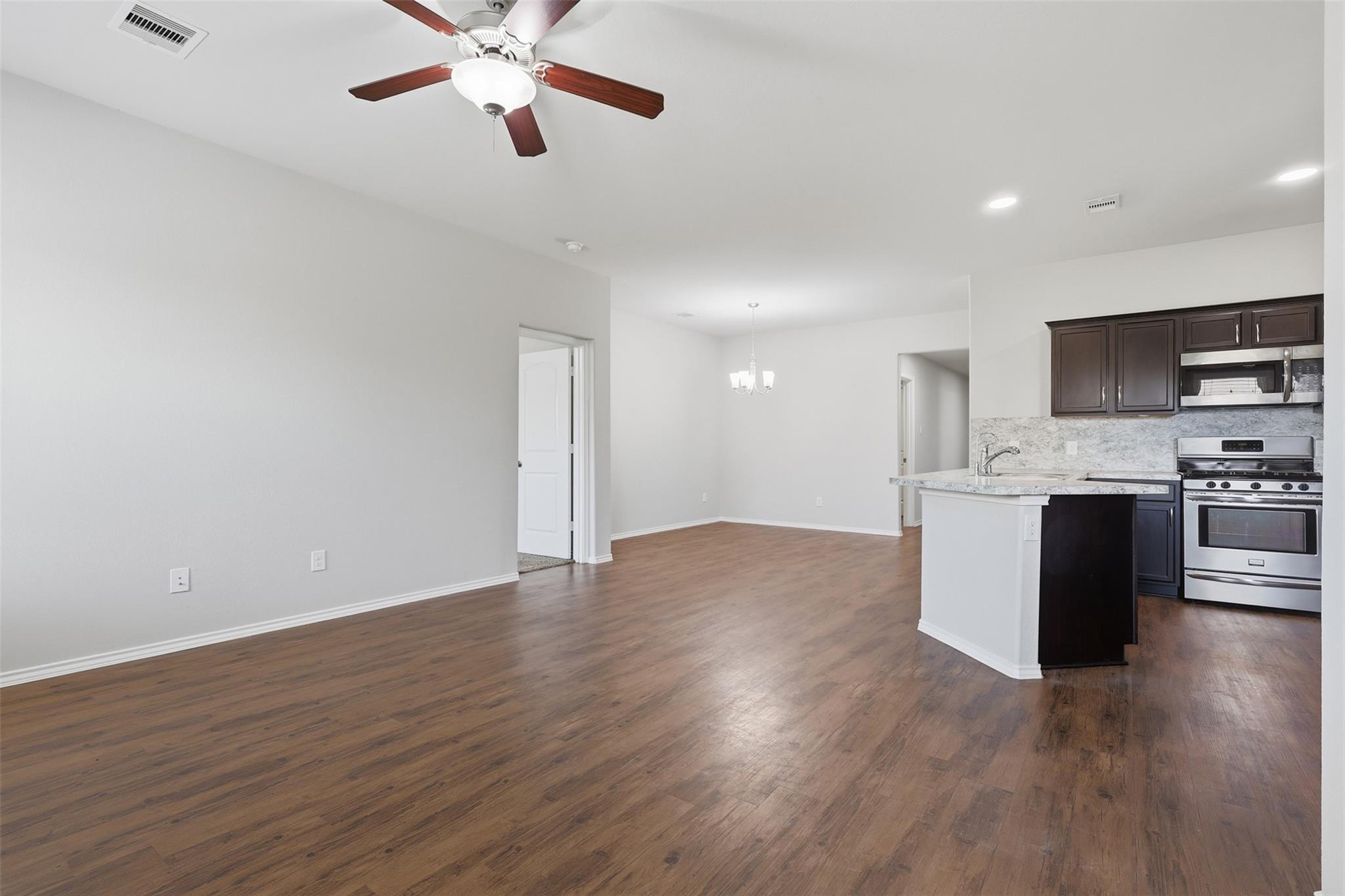 Open-plan living and dining area with wood-look floors, opening to a kitchen with dark cabinets and stainless steel appliances.