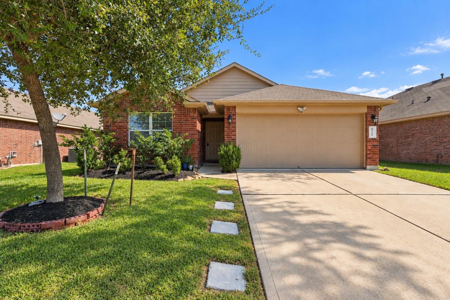 Brick house with an attached two-car garage, broad driveway, and mature tree in the front yard.