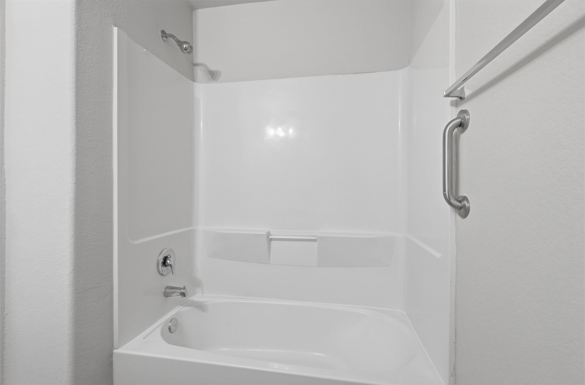 Bathroom tub and shower with a built-in shelf and chrome grab bar.