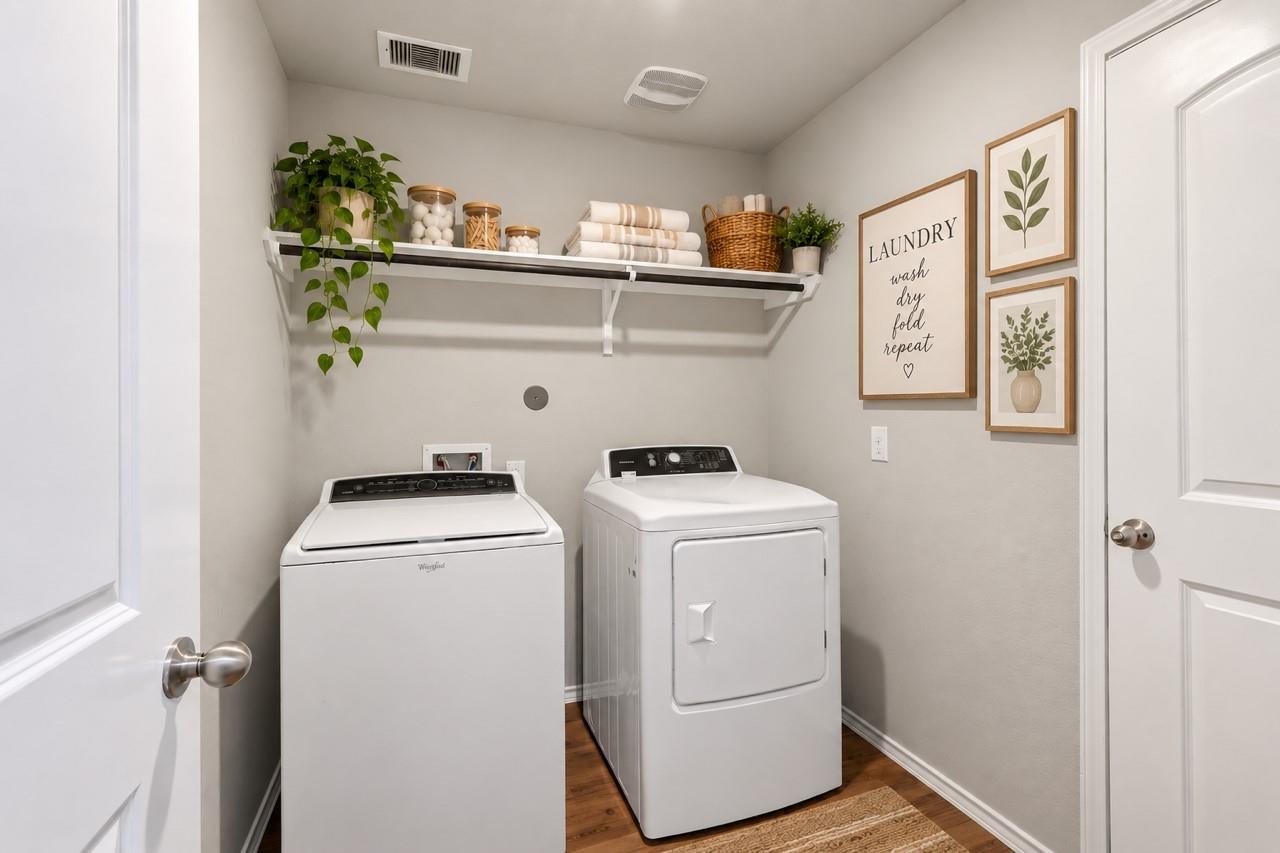 Laundry room with a white washer and dryer, styled shelf, and framed botanical prints.