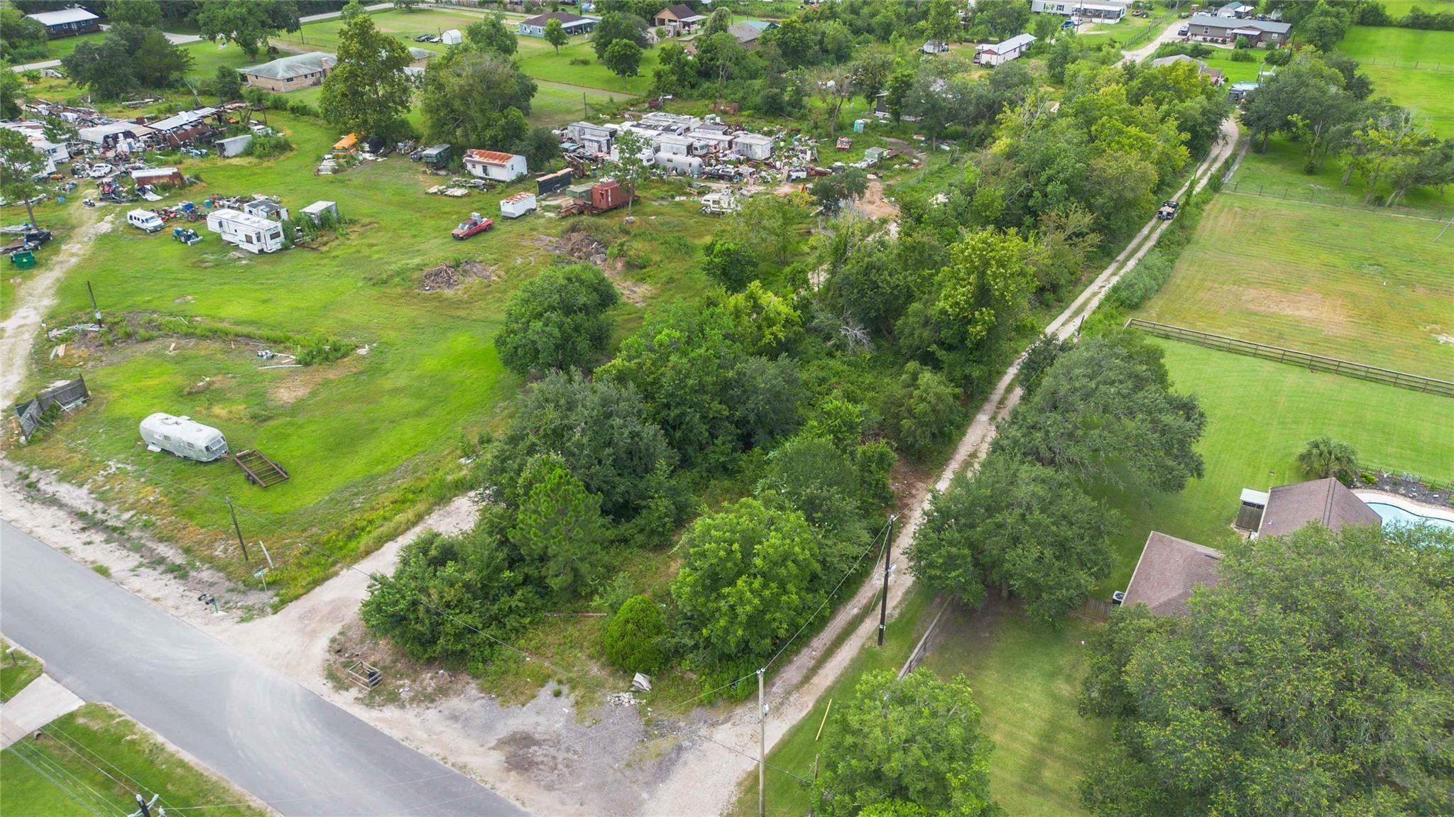 Aerial view of a grassy lot with scattered trailers and sheds beside a tree-lined dirt lane.