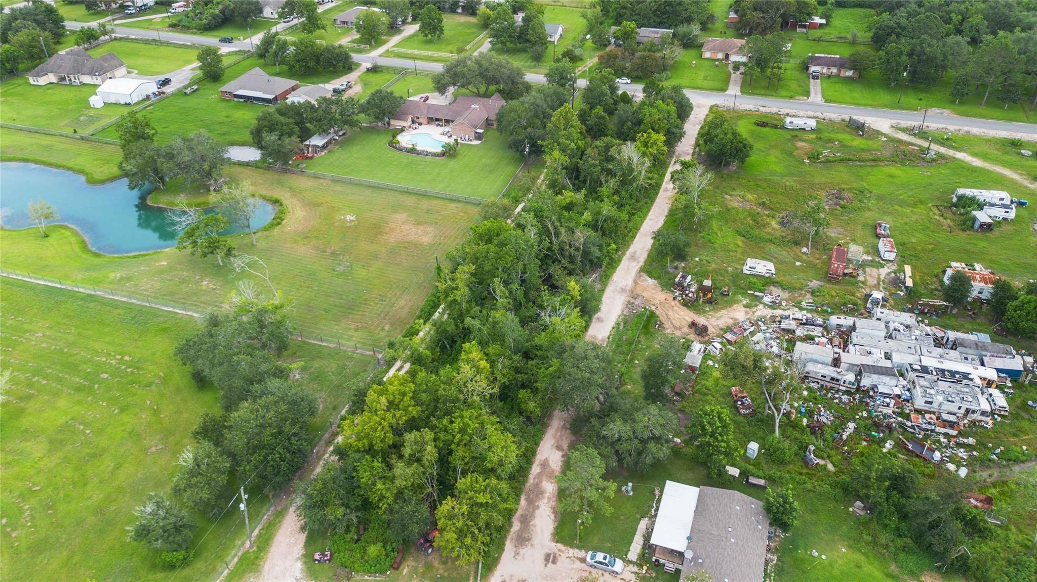 Aerial view of a rural home with a swimming pool, pond, and expansive grassy grounds.