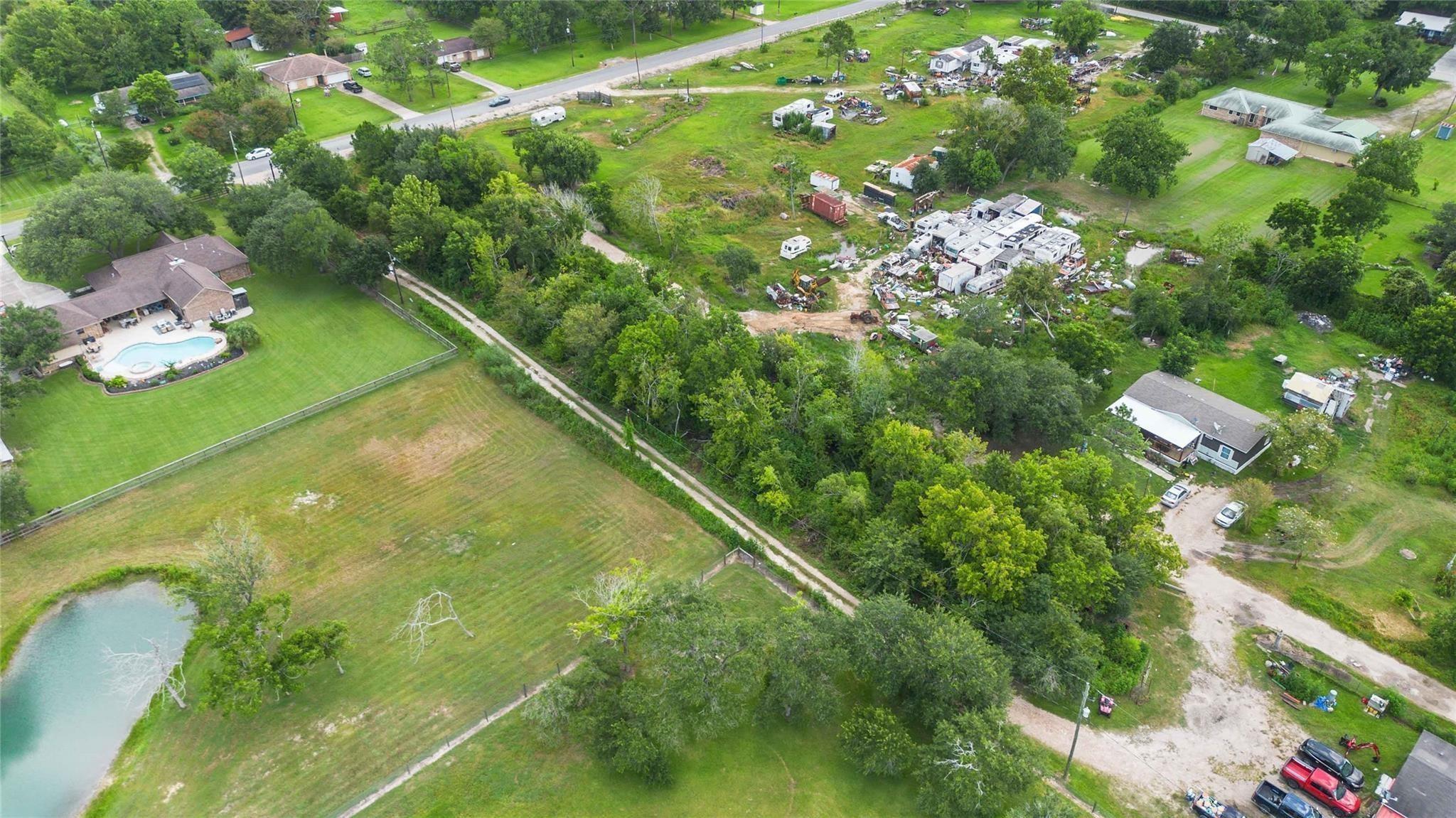Aerial view of a property with a pond, lawns, trees, and a cluster of trailers and equipment.
