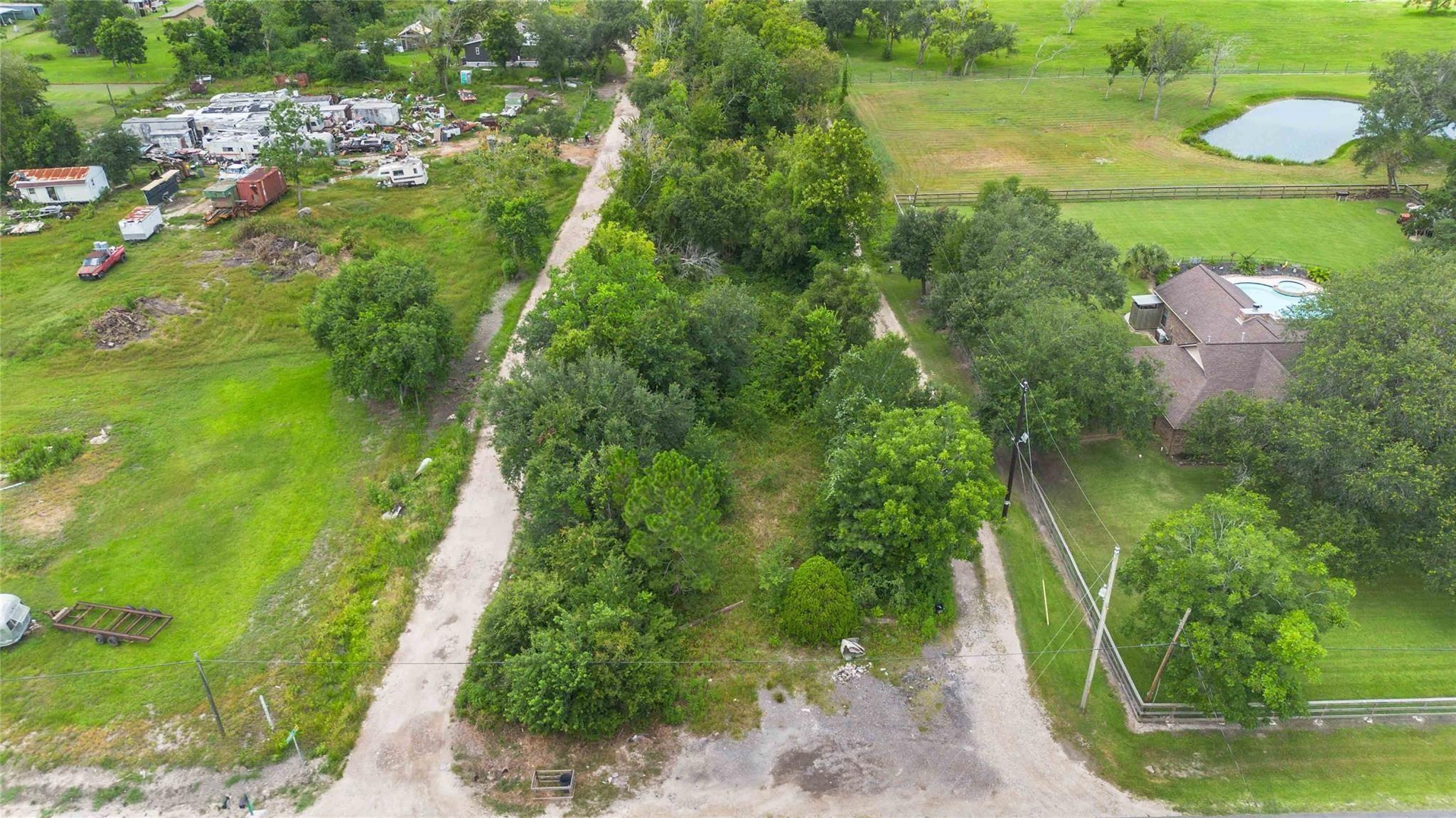Aerial view of a tree-covered property with gravel lanes, a nearby pond, and a neighboring home.