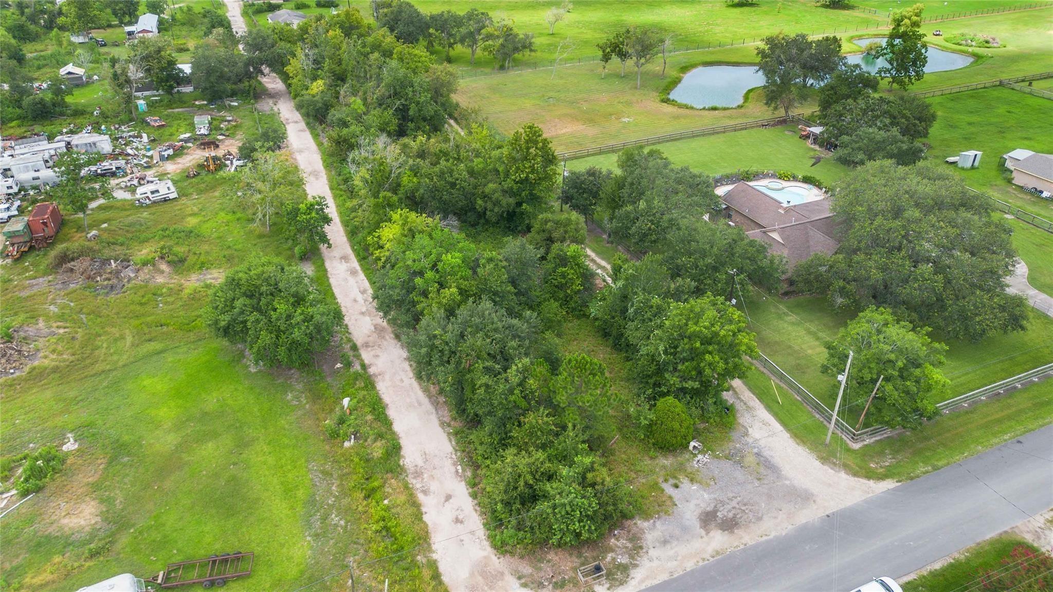 Aerial view of a wooded property with a house, swimming pool, fenced grounds, and two ponds.