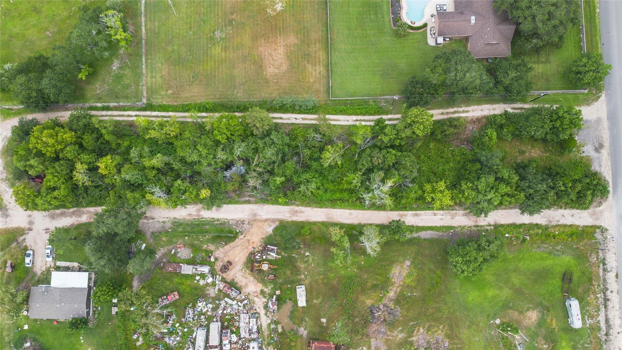 Aerial view of a wooded strip beside open yards, with nearby homes, a pool, and roads.
