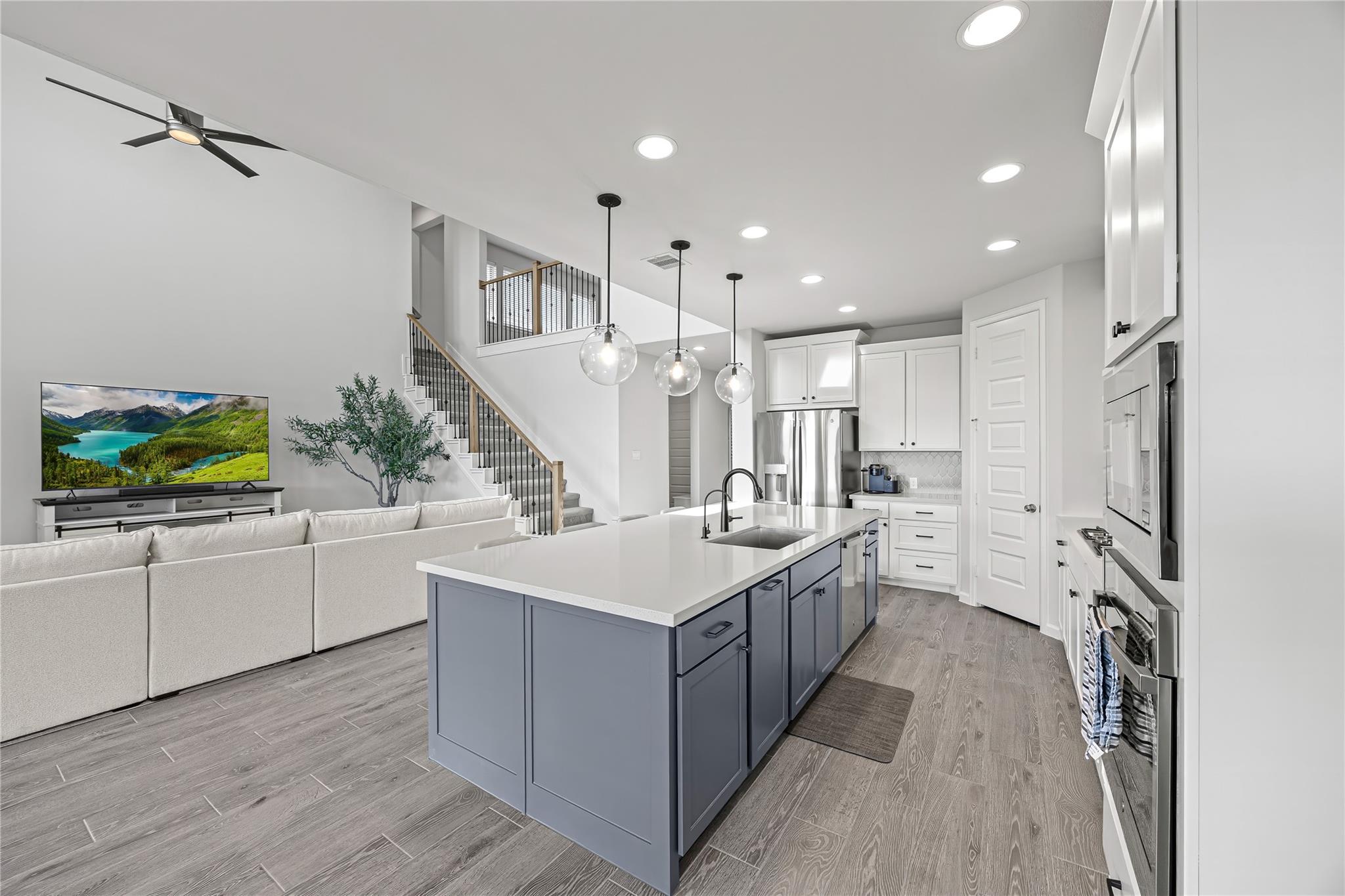Open kitchen and living area with a blue-gray island, stainless appliances, and a staircase.