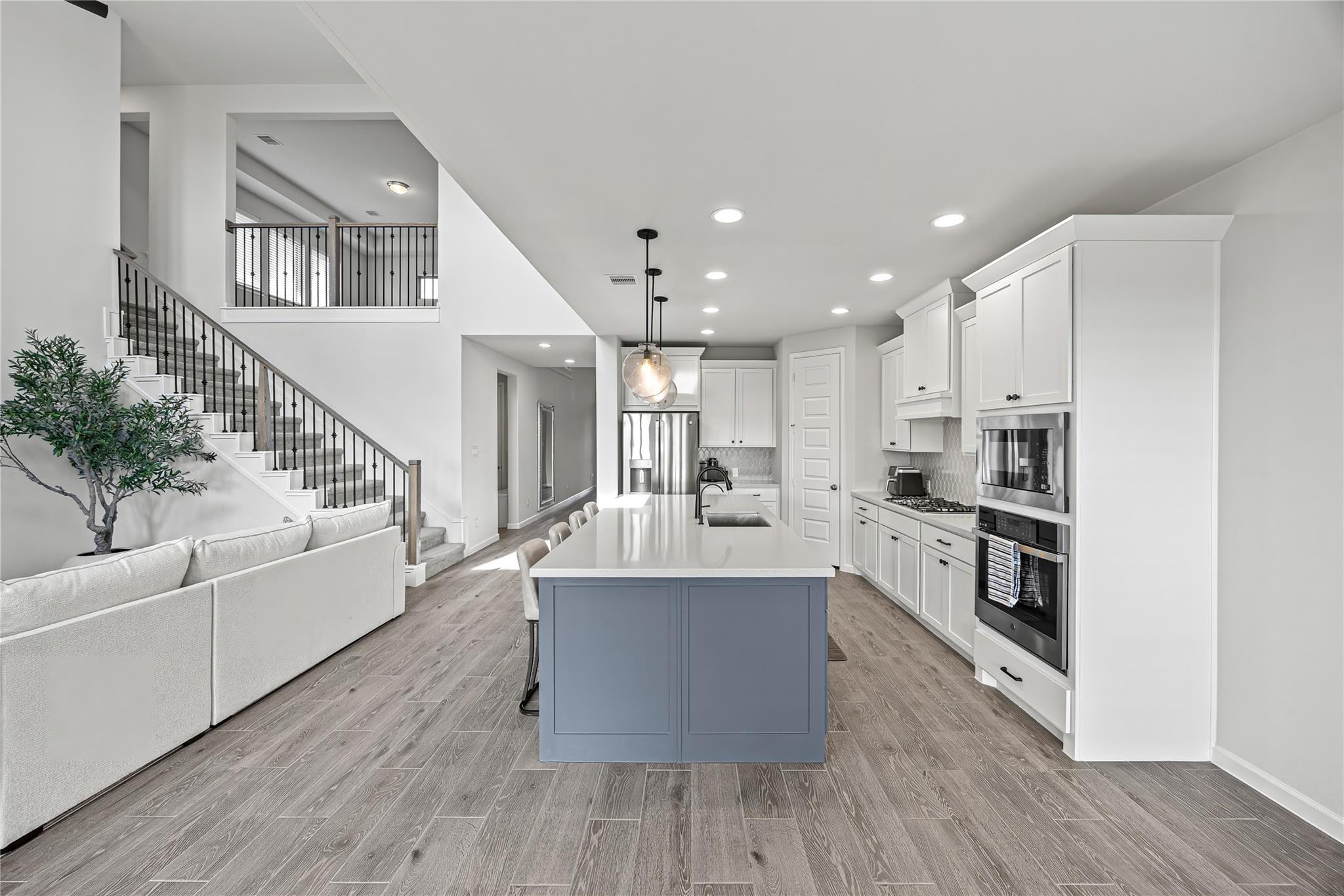Open-concept kitchen with a blue-gray island, white cabinets, stainless appliances, and a staircase beside the living area.