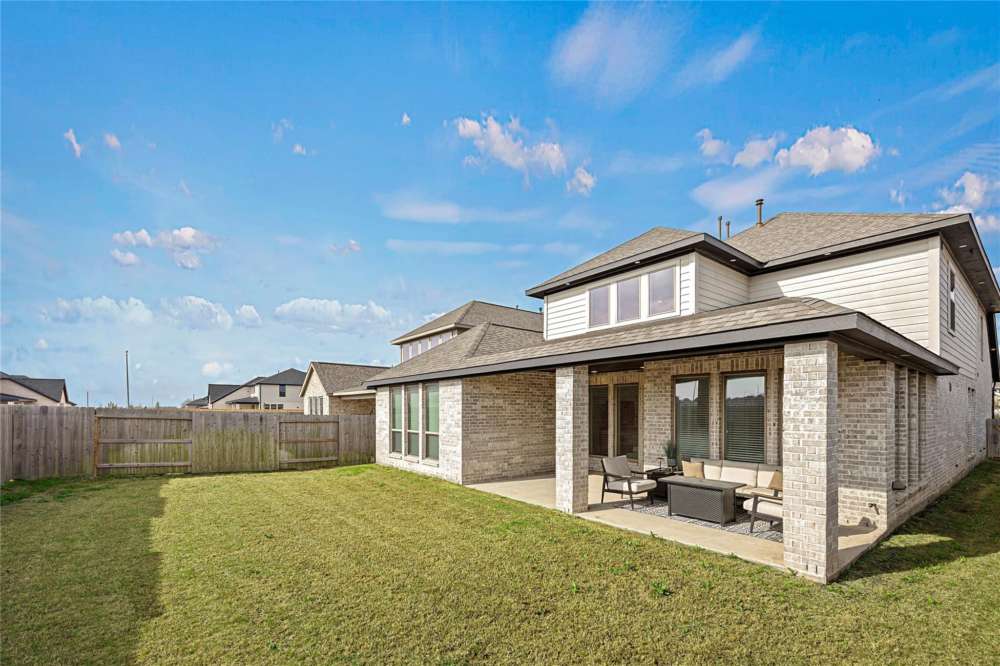 Two-story home with a covered, furnished patio overlooking a fenced grassy backyard.