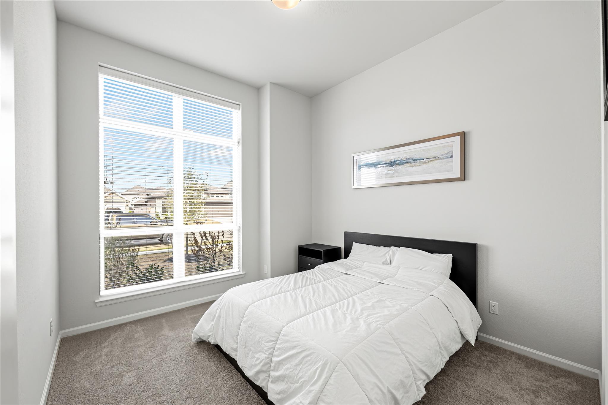 Bedroom with a white bed, black headboard, and large window with blinds.