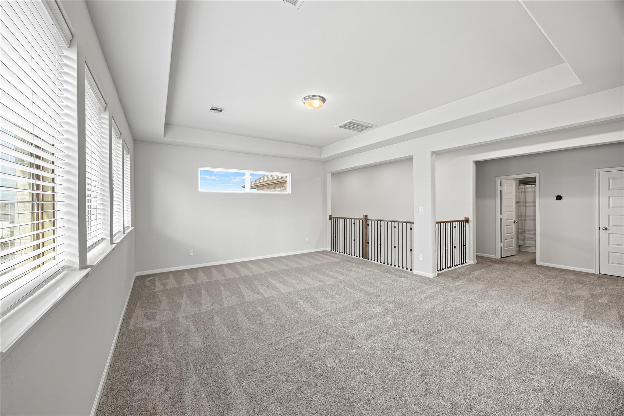 Empty carpeted upstairs loft with wide windows and a black metal railing overlooking the lower level.