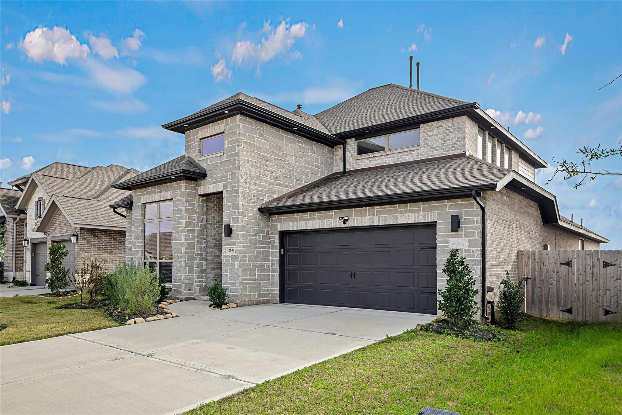 Two-story gray stone house with a dark double garage, broad driveway, and landscaped front yard.