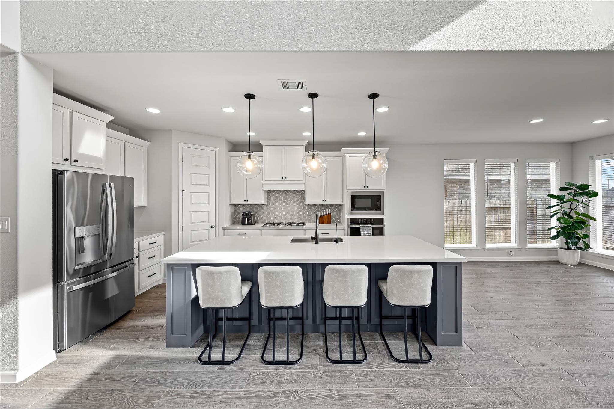 Modern kitchen with a large island, four stools, white cabinetry, and stainless steel appliances.