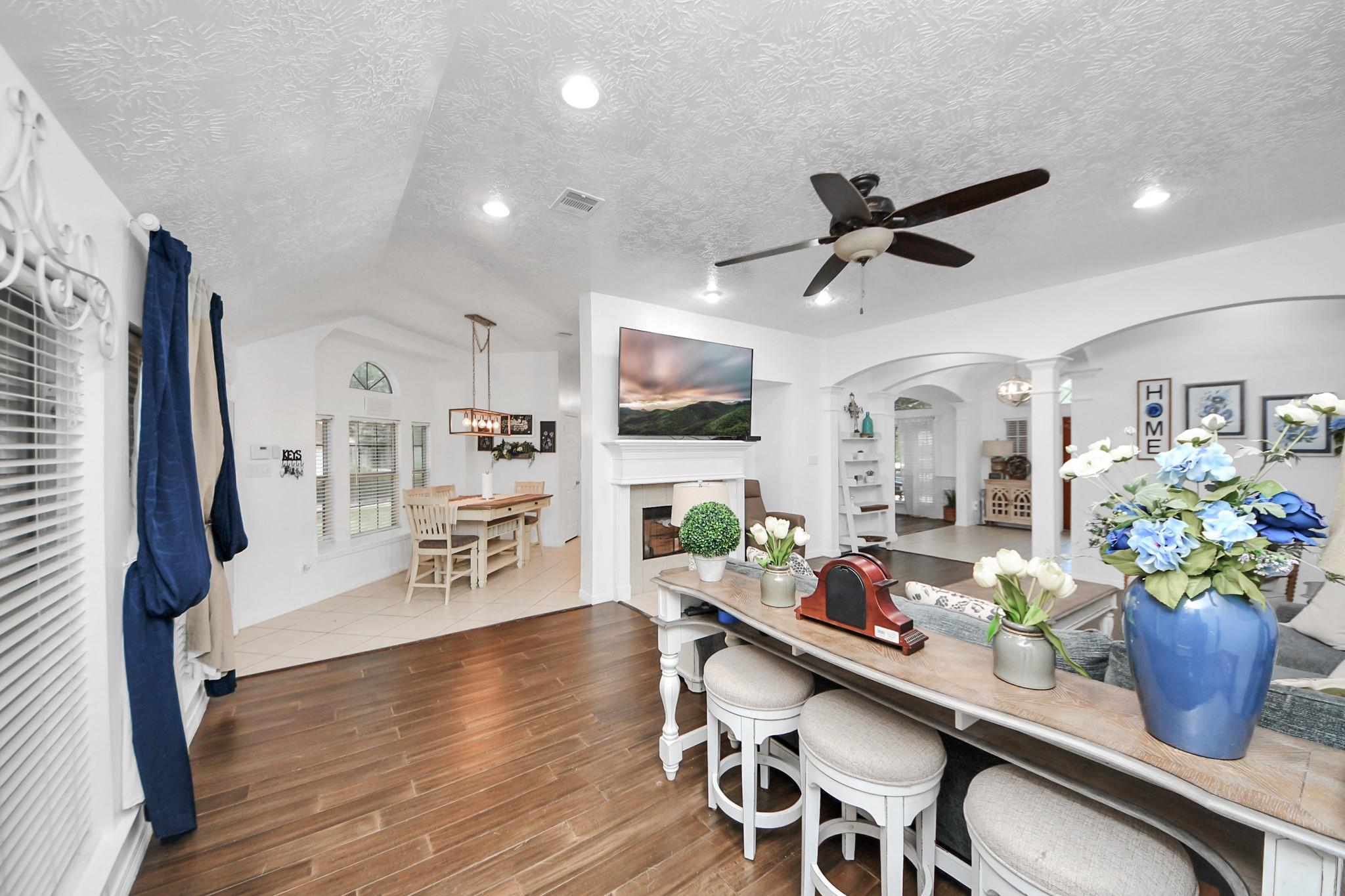 Open-plan living and dining area with a white fireplace, dark wood floors, and blue-and-white flowers on a console.