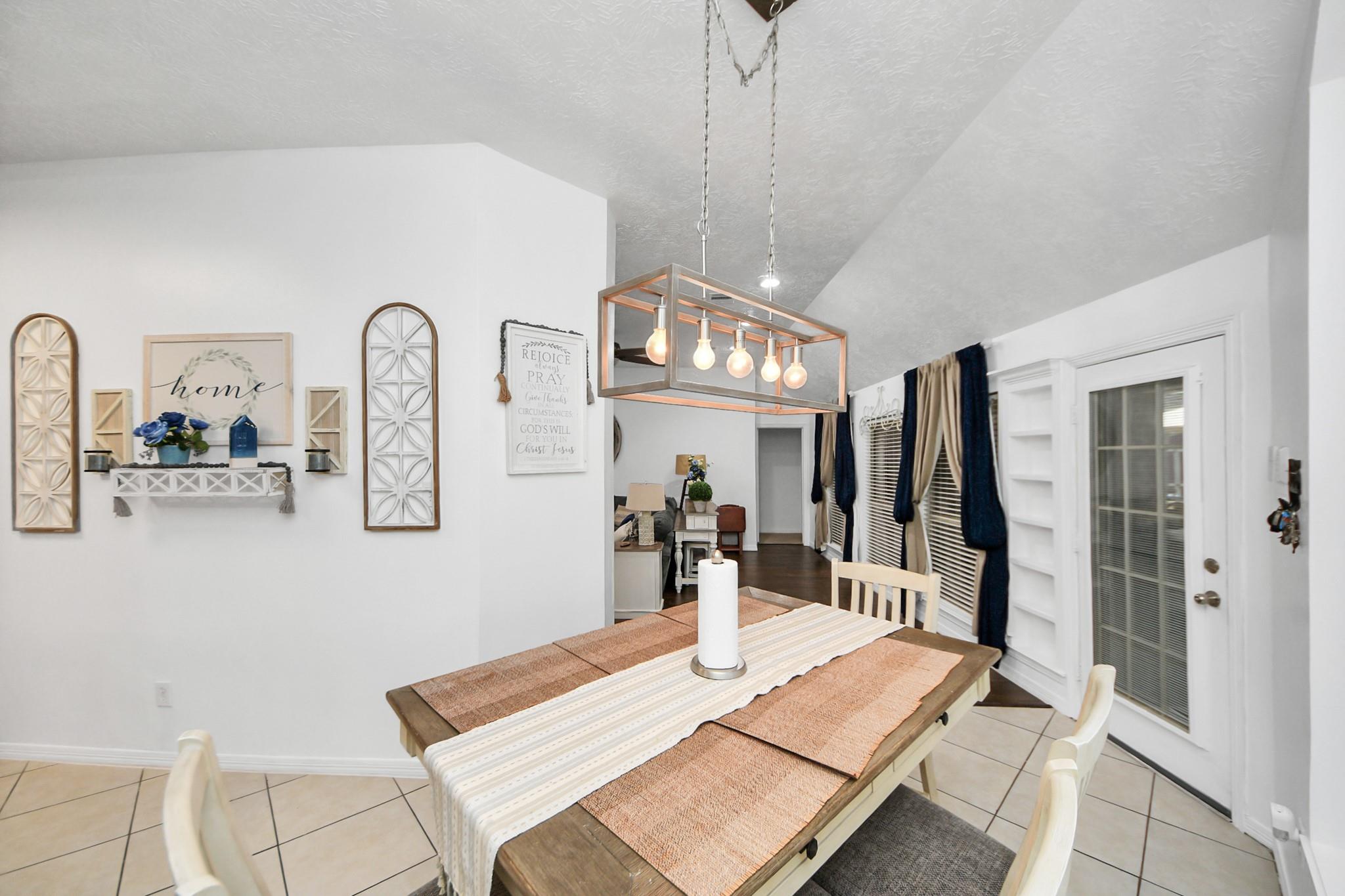 Dining room with a rustic wood table, striped runner, and exposed-bulb pendant light.