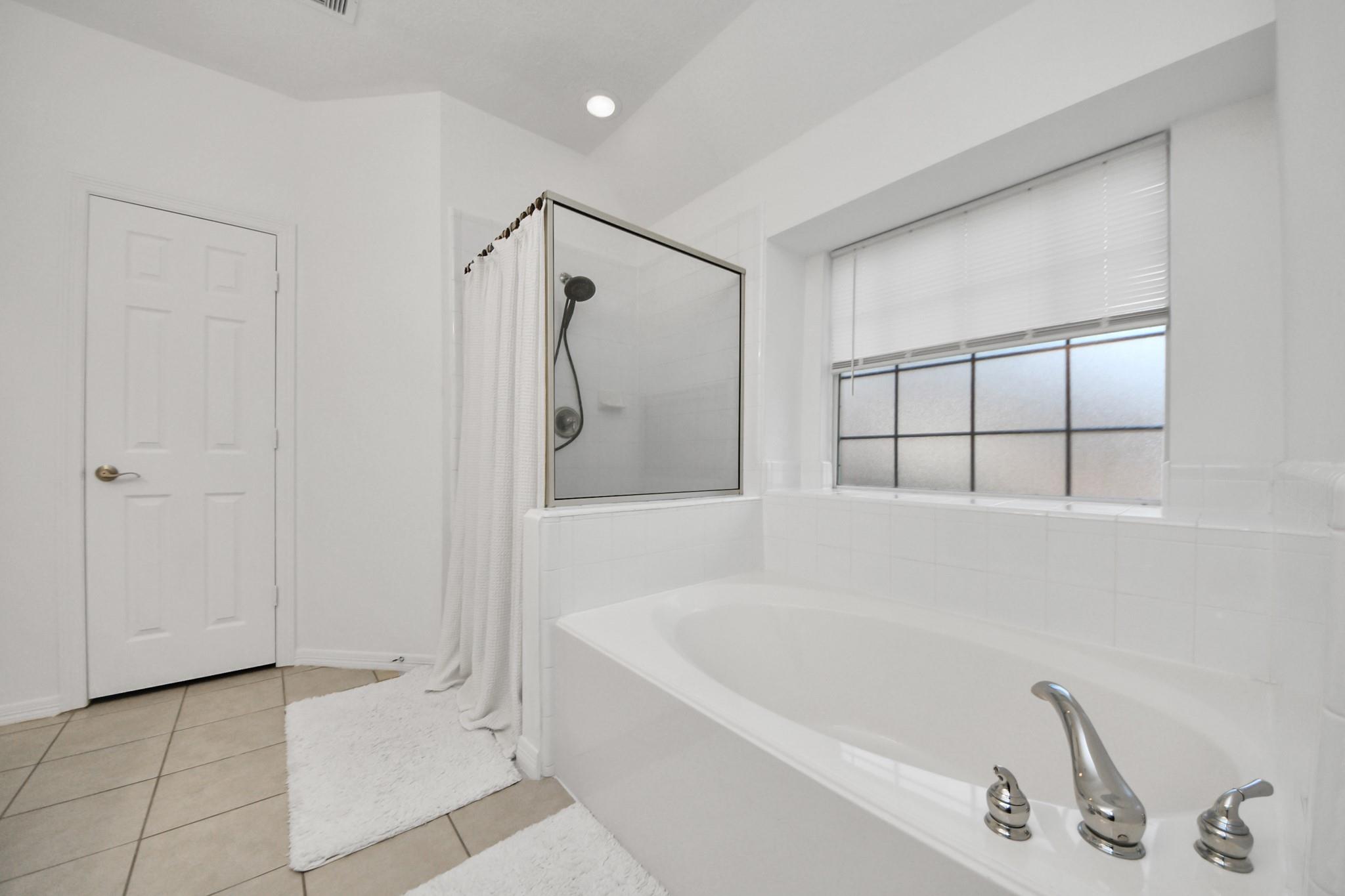 Bathroom with a built-in tub, glass shower enclosure, and large window with blinds.