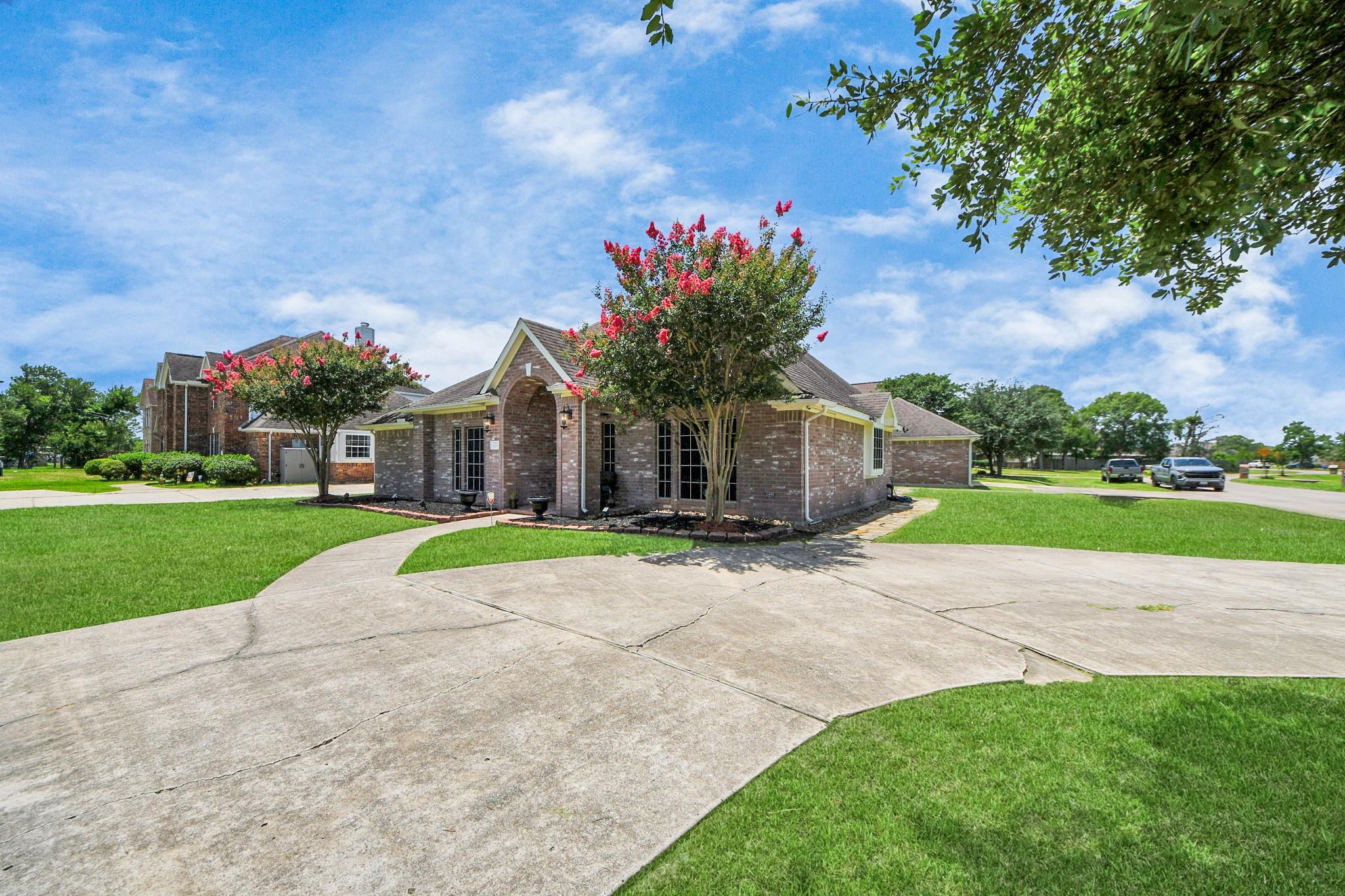 Brick home with a broad concrete driveway, green lawn, and pink-flowering trees.