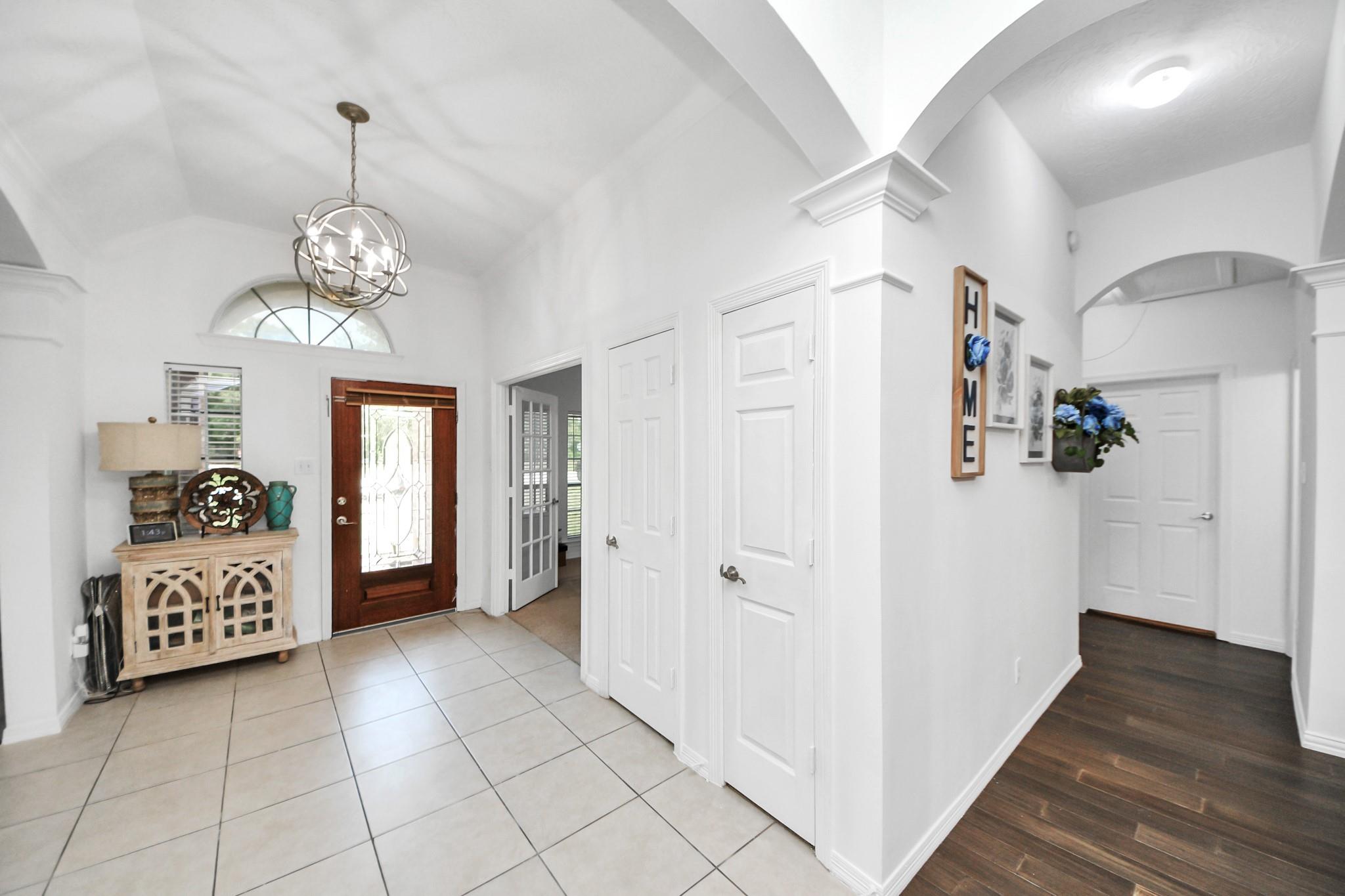 Entry foyer with a vaulted ceiling, globe chandelier, tiled floor, and dark wood front door with decorative glass.